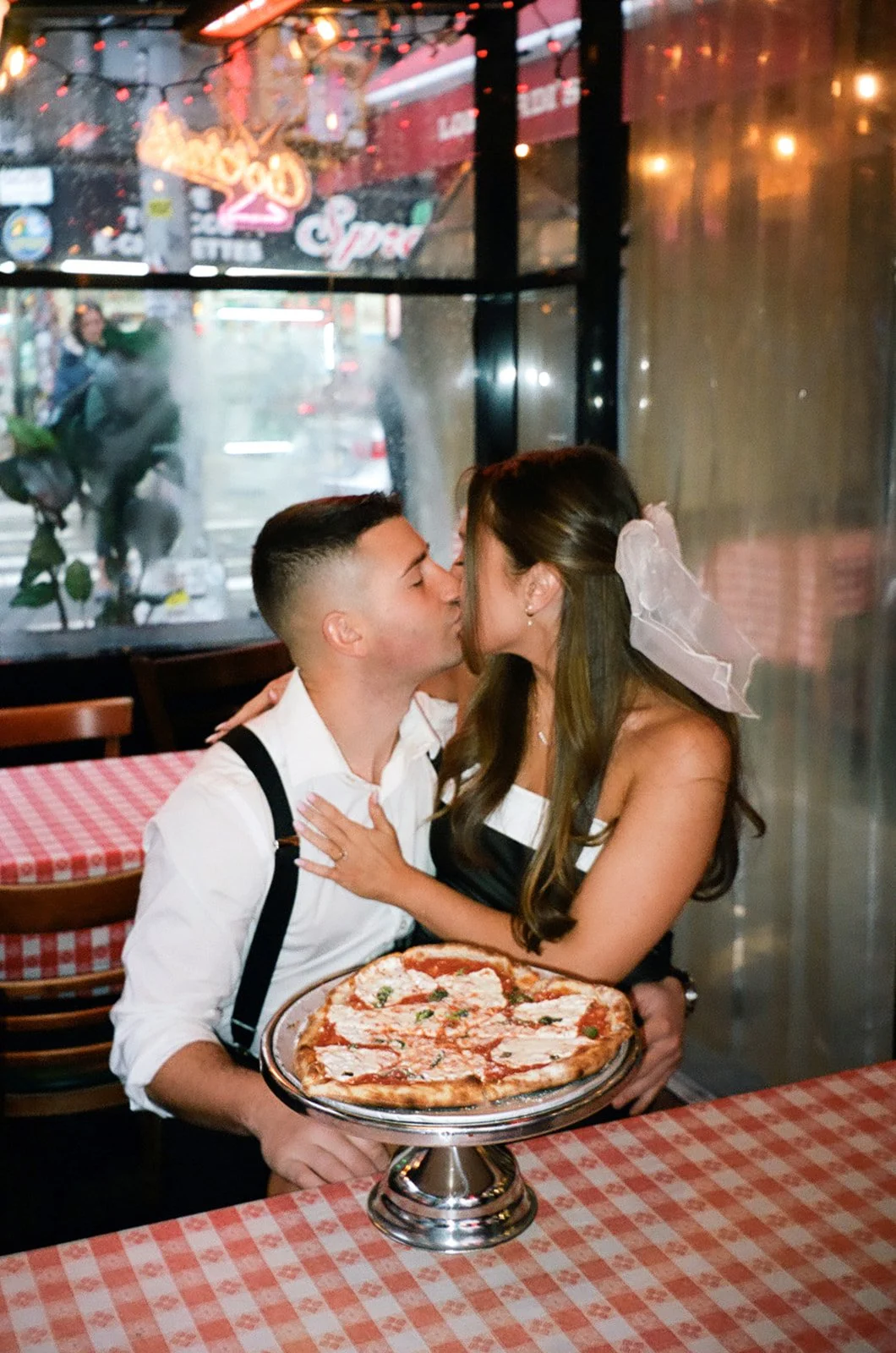 Couple kisses at a pizzeria with a heart shaped pizza on the red and white checkerboard table