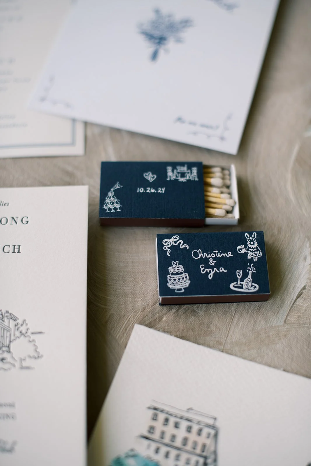 flatlay closeup of pieces of stationery and matchboxes with custom wedding designs