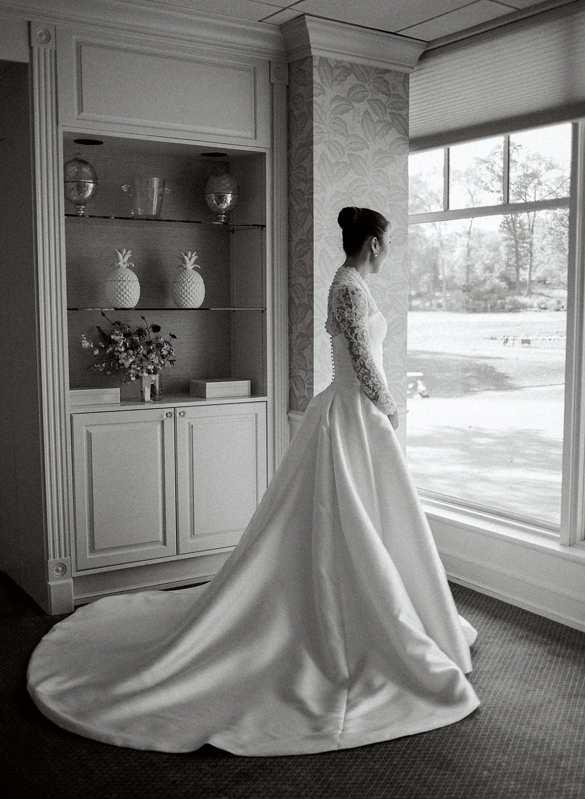 Full length portrait of a bride looking out a large window with her ballgown spread out around her