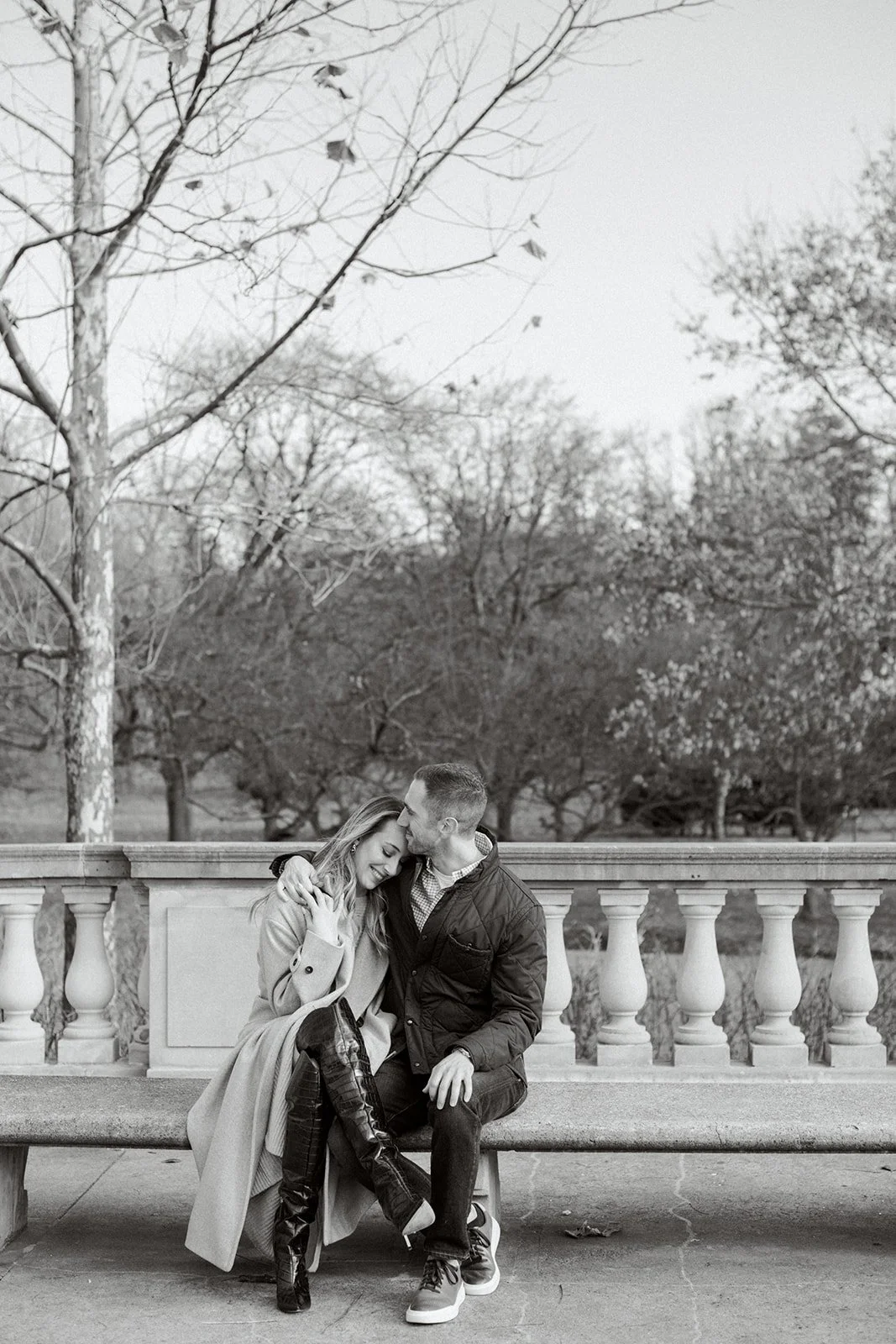 Couple sits close to each other as man kisses woman's head. Black and white image.