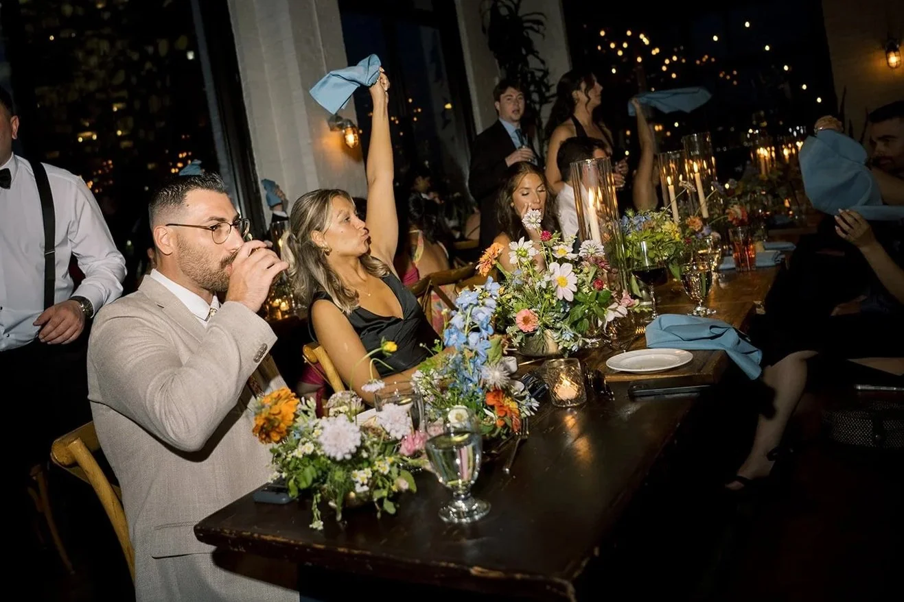 wedding guests at long tables waving blue napkins