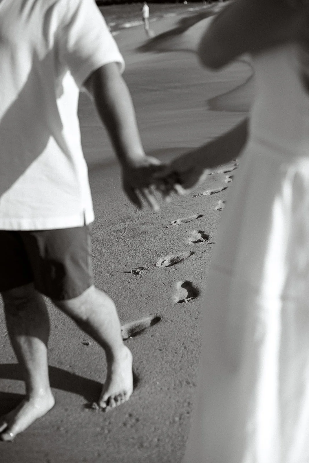 Couple holding hands with foot prints in the sand behind them