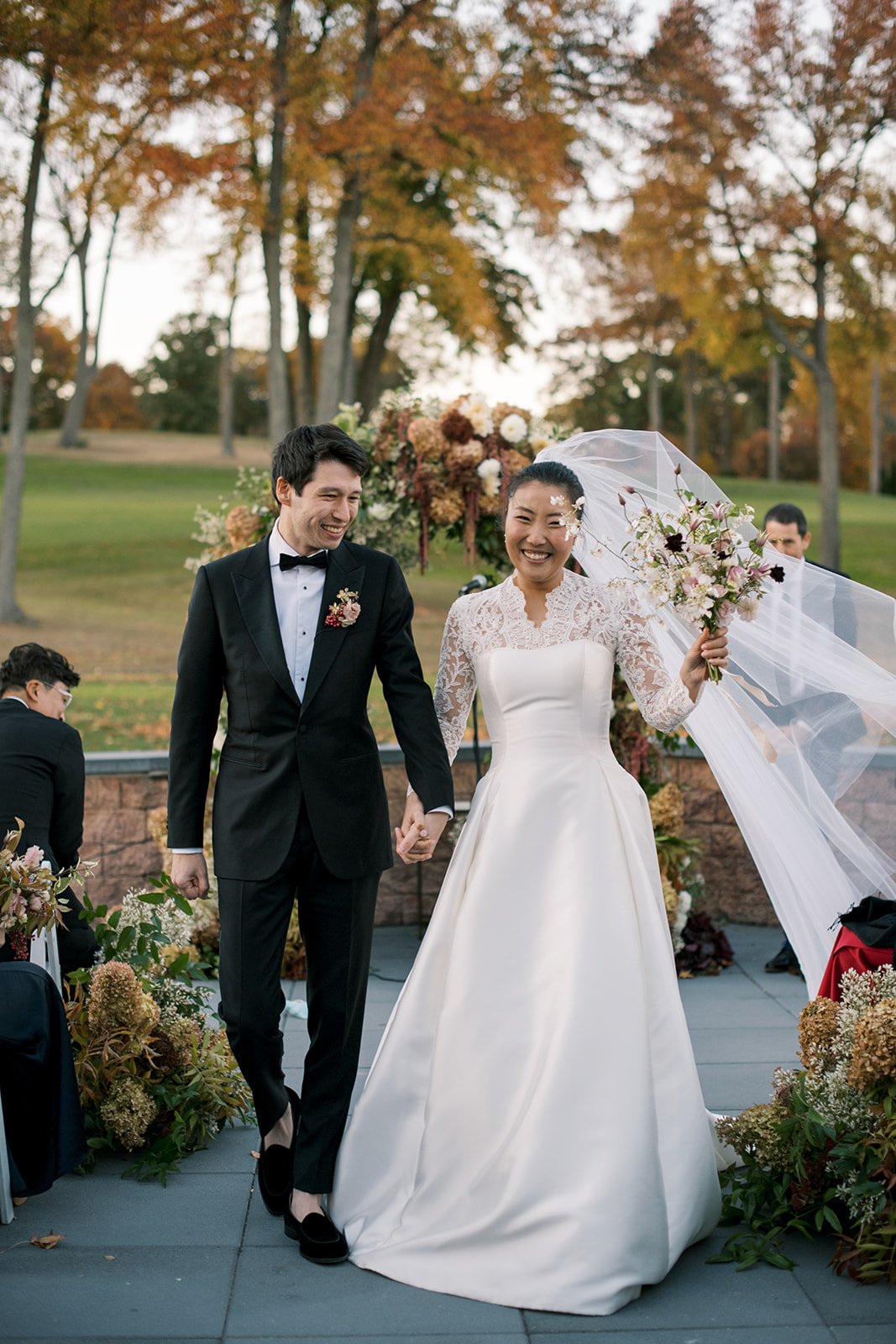 bride and groom proceeding down the aisle. bride smiles at camera with her veil flowing in the wind and the groom smiles at the guests