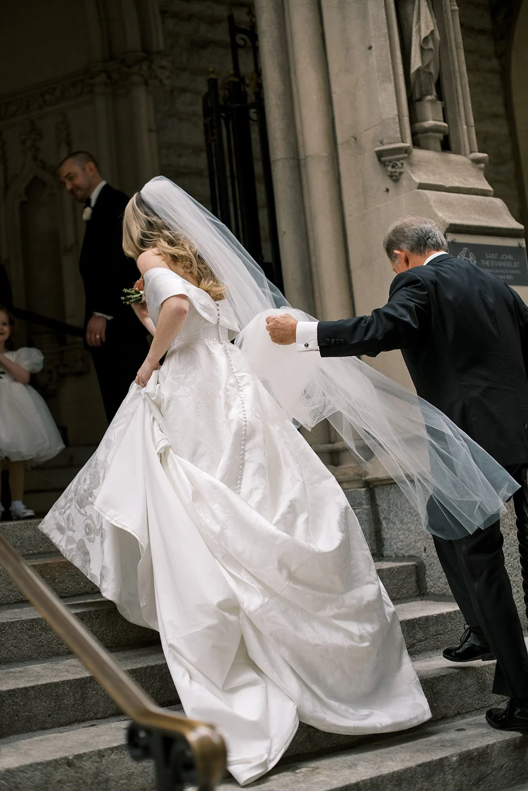 Father of bride holding veil as he and bride ascend church stairs