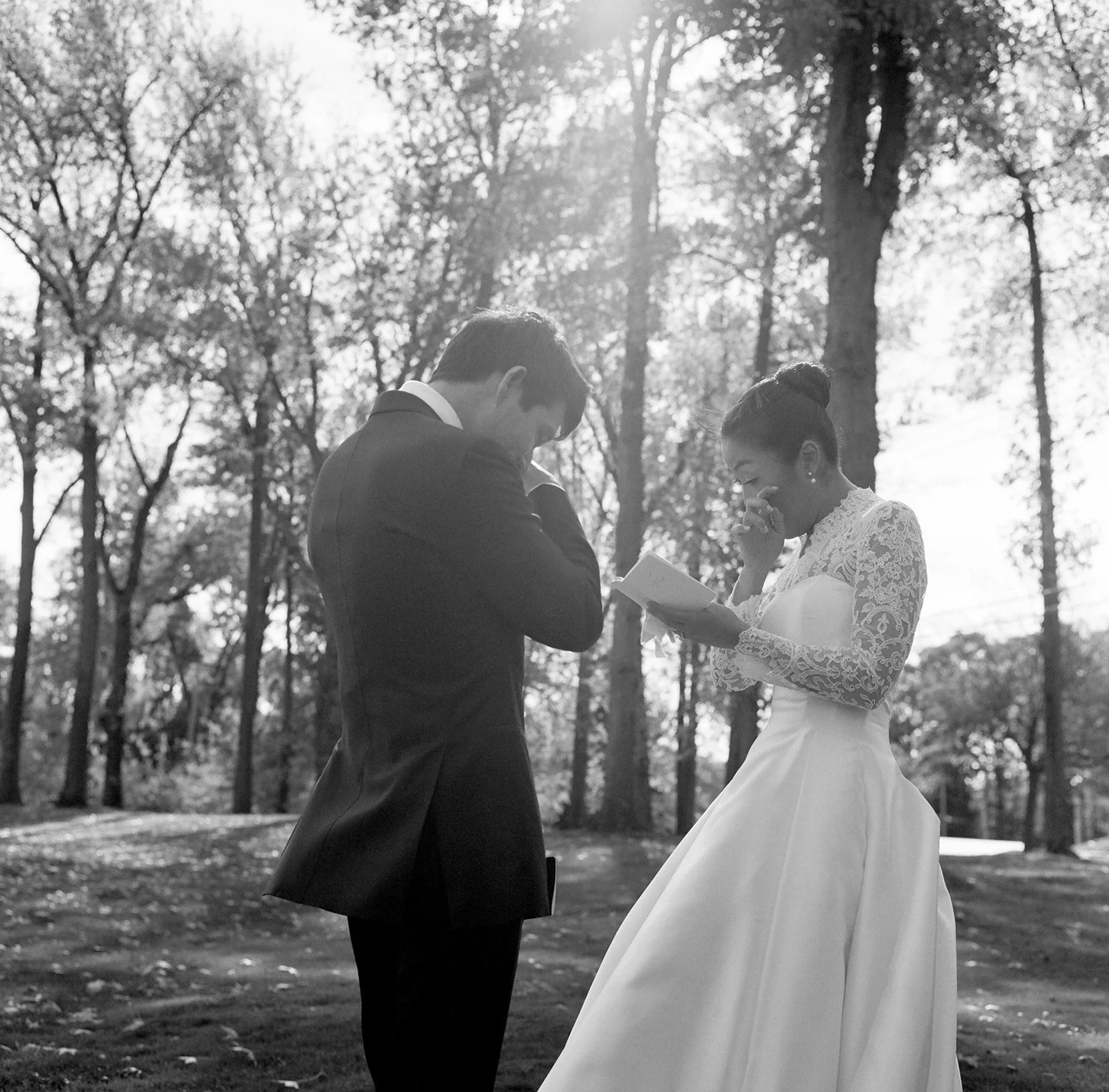 black and white film image of bride and groom wiping tears as the bride reads from her vow book