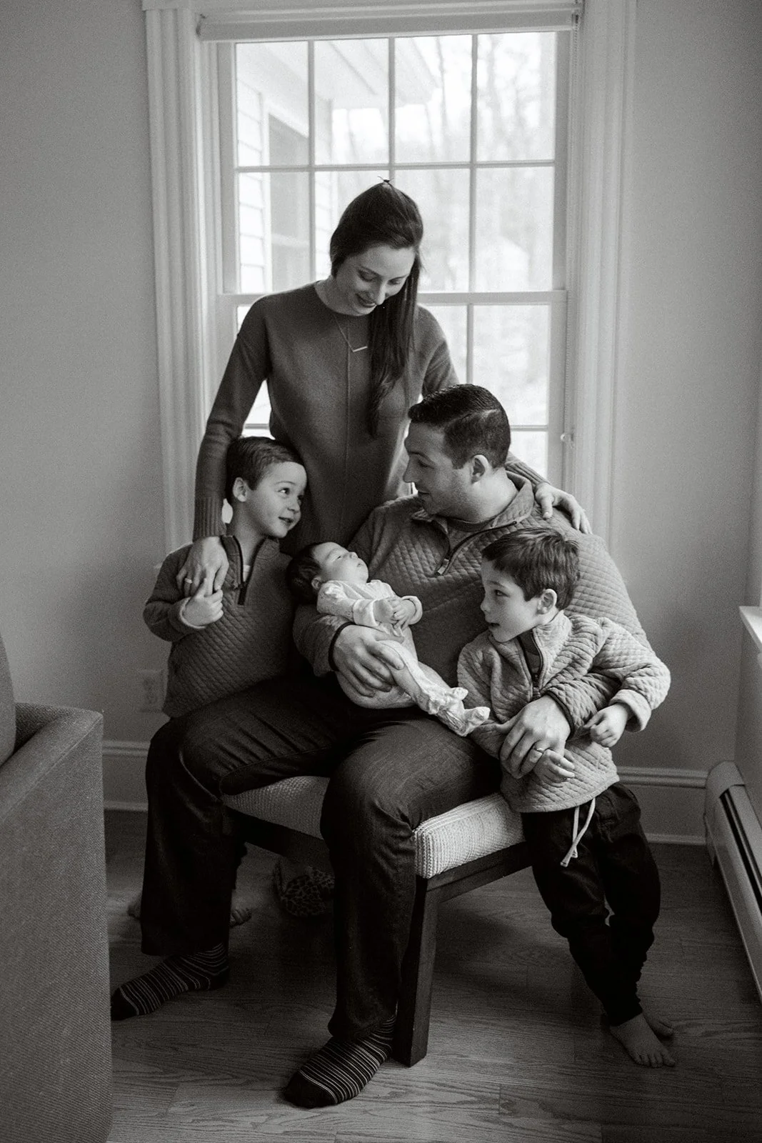 Family of 5 stands for a portrait together. Dad holds newborn baby as mom stands with twin toddlers. Black and white image.
