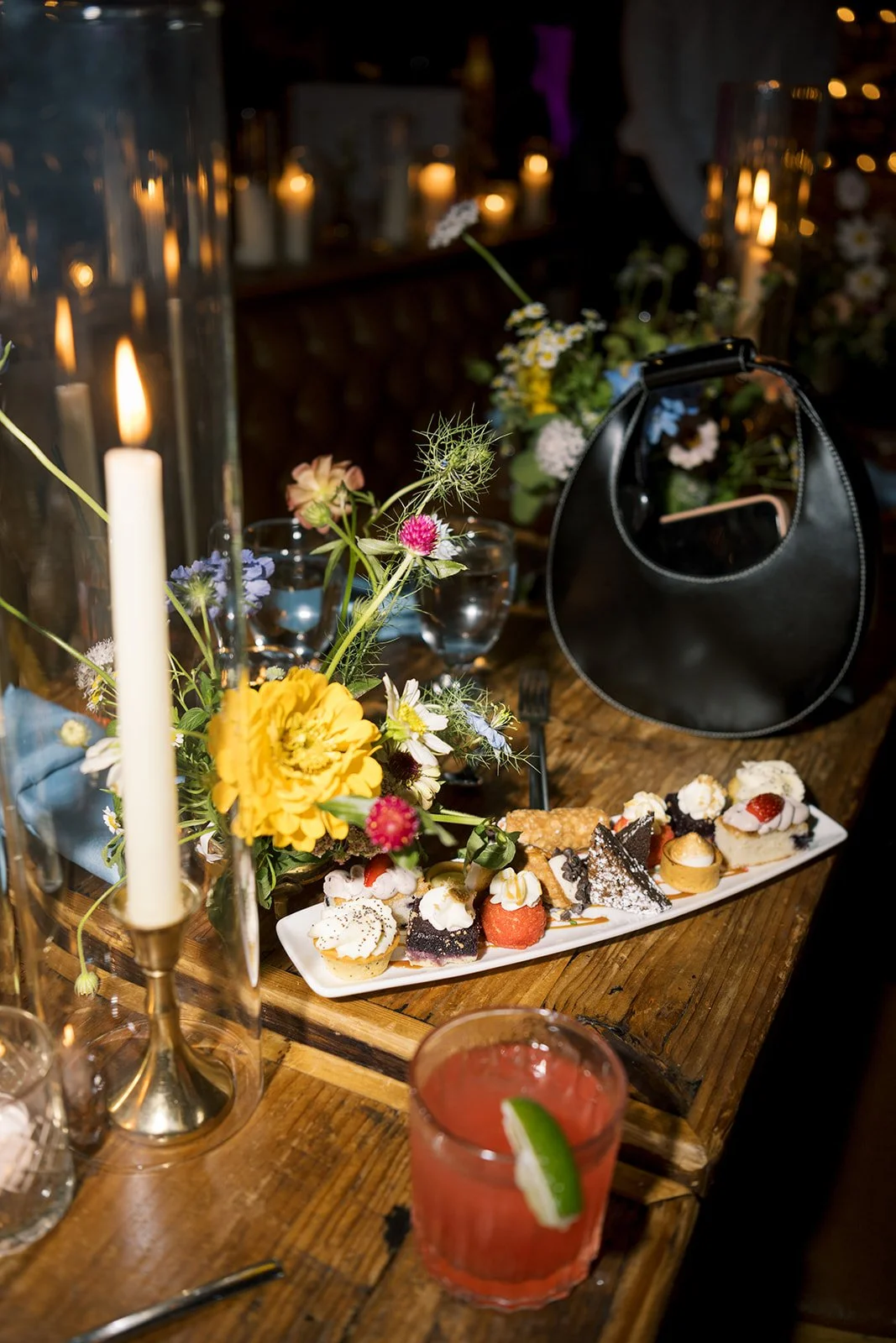 detail photo of reception table with plated  mini desserts, red cocktail drink, and black purse
