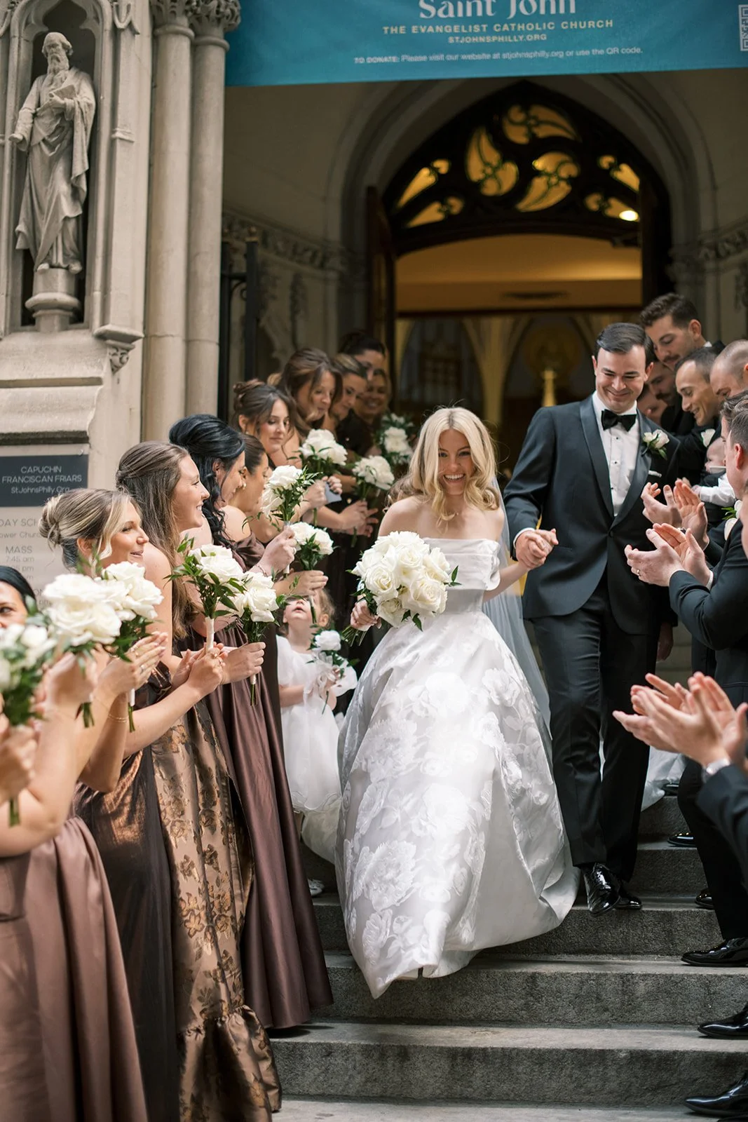 bride and groom exit church with wedding party on the sides