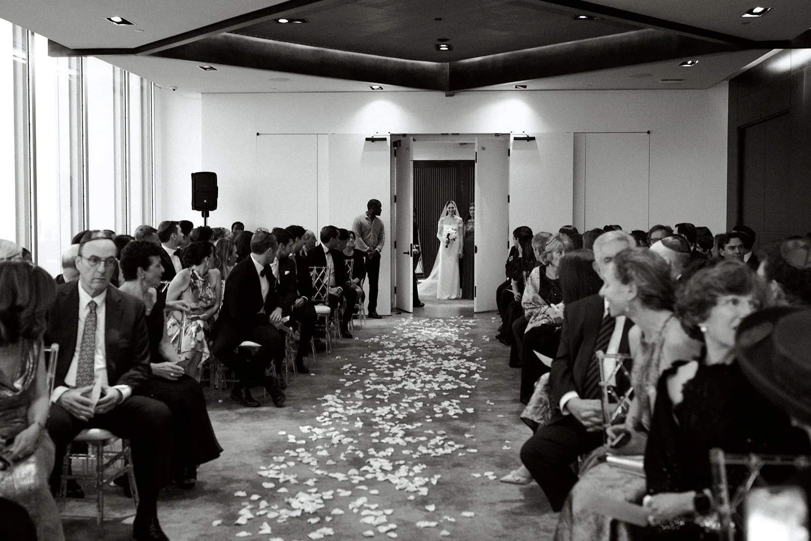 guests looking down the petal strewn aisle as the doors open to reveal the bride and her mother 