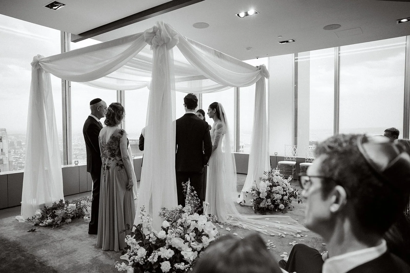 Jewish ceremony at Manhatta. Chuppah draped with chiffon and large floral arrangements on the floor