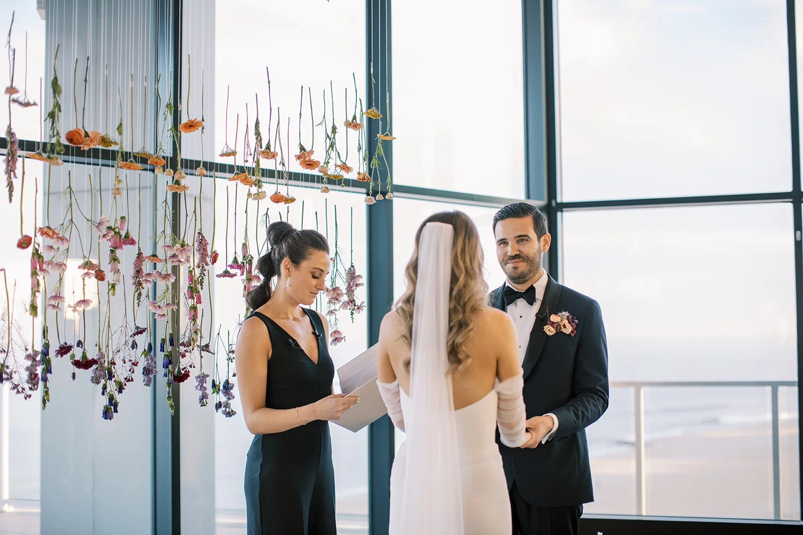 Indoor wedding ceremony at Wave Resort with floral installation behind bride and groom