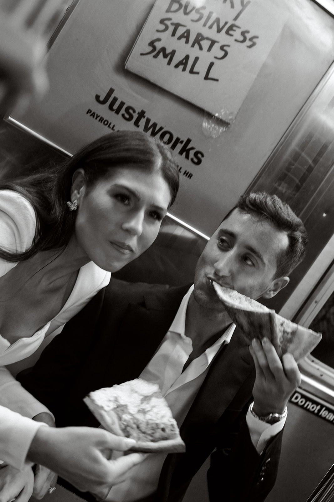black and white image of a couple eating slices of pizza on the subway in NYC