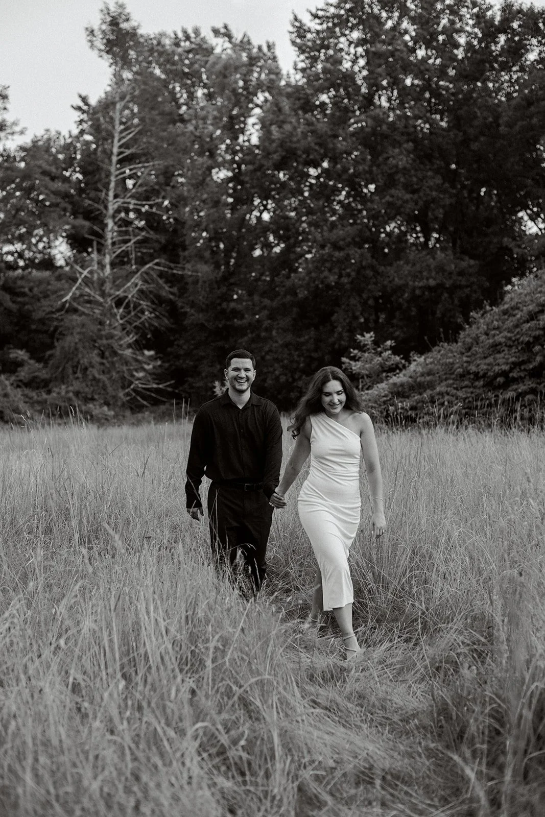 Couple walking together holding hands through tall grasses. Black and white image