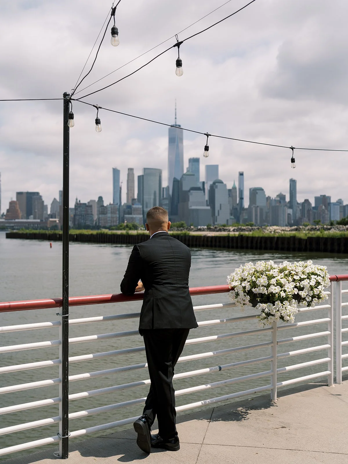 back of groom leaning against a railing overlooking the NYC skyline. Battello wedding