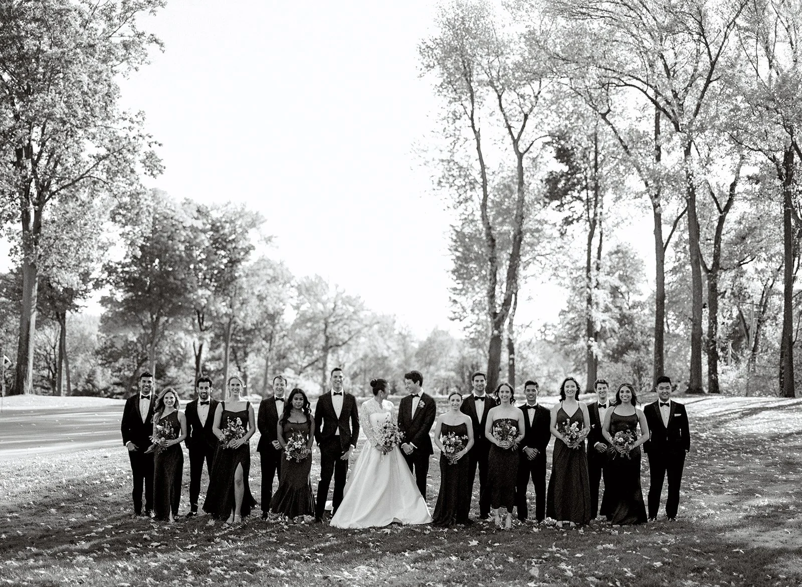 Wedding party group photo at North Hills Country Club. Wedding party stands in a line with bride and groom standing in the center, looking at each other. Black and white image