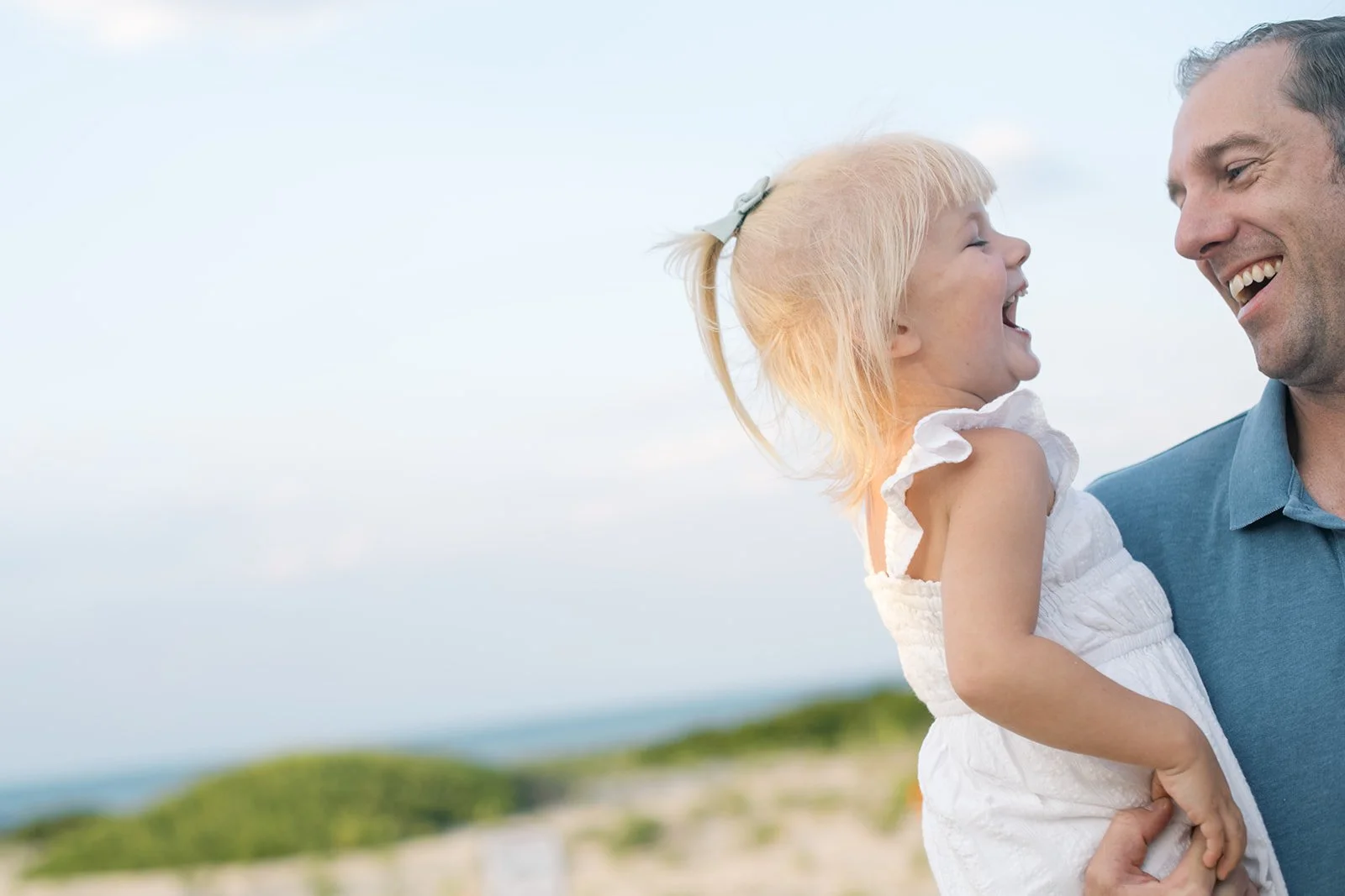 Beach setting in the background with man holding a young girl laughing together