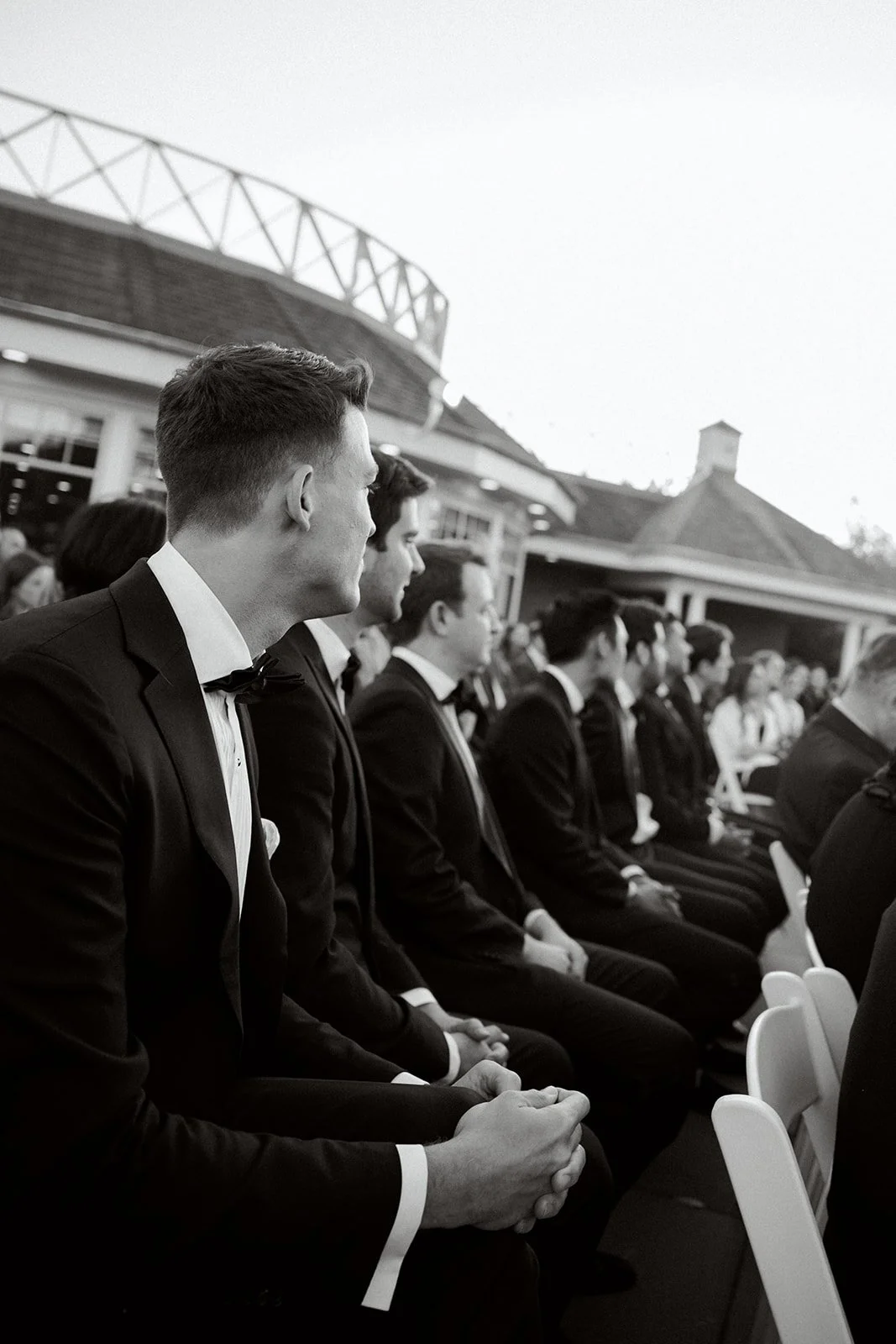 photo down the row of seated groomsmen watching a wedding ceremony