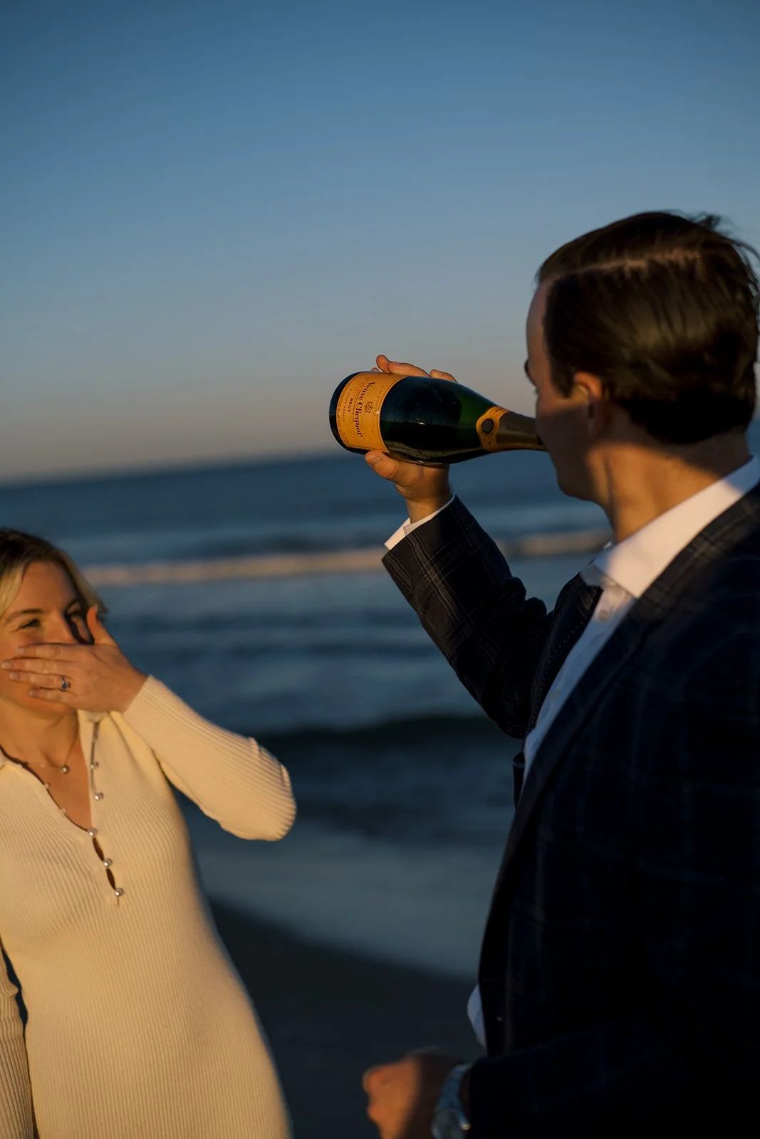 Sunset lighting at the beach as a couple shares a bottle of champagne together.