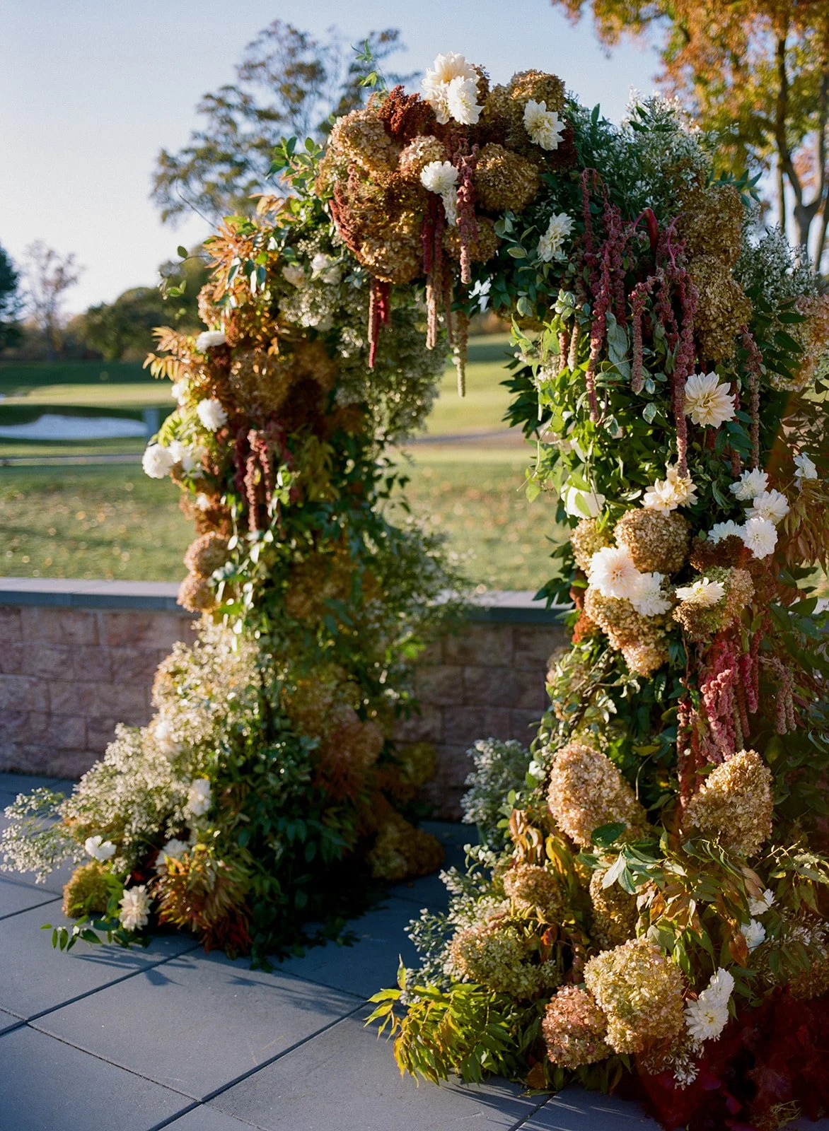 Large floral arch filled with greens, mauve, and maroon flowers.