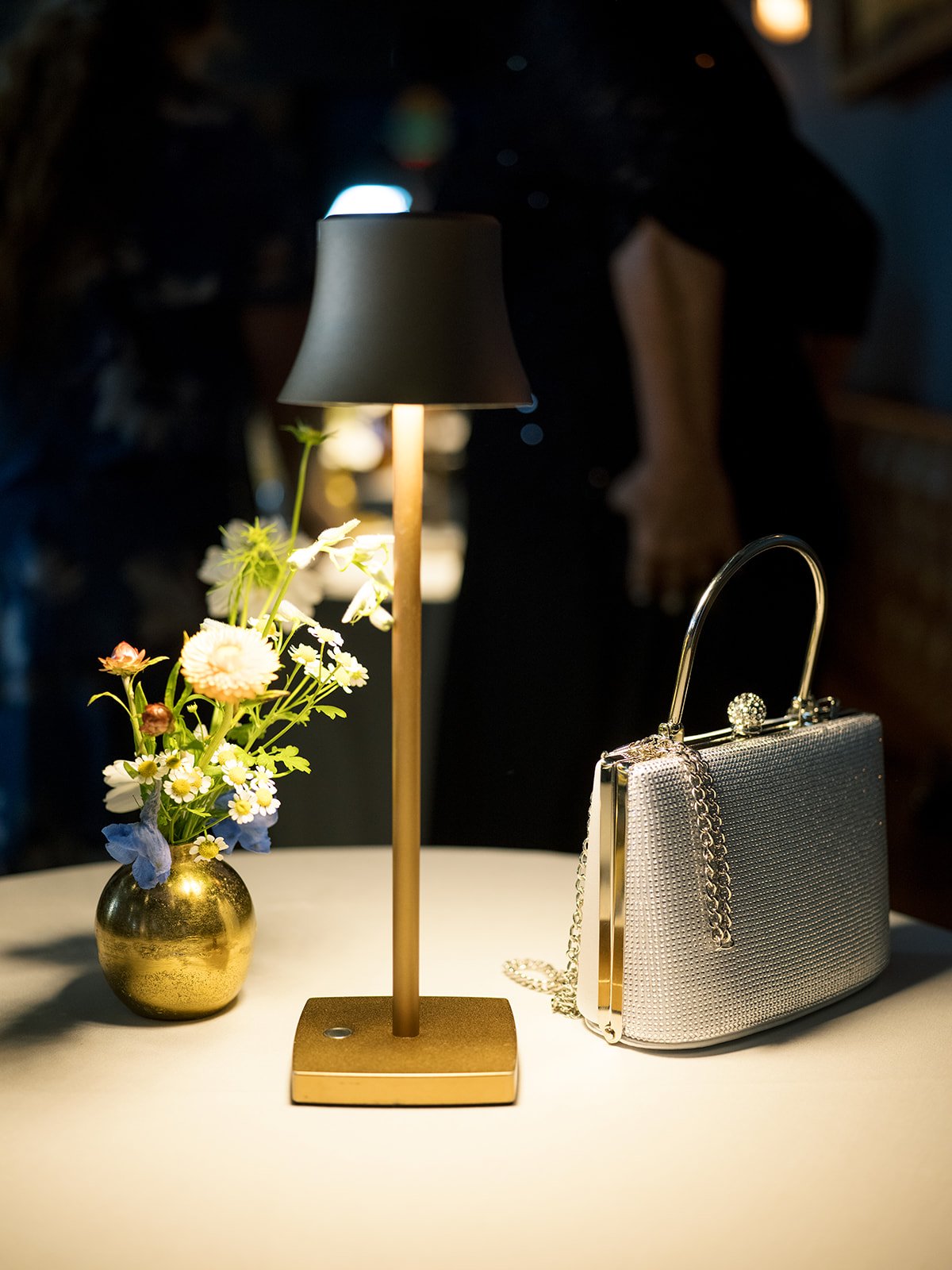 detail photo of table lamp, small floral arrangement, and silver handbag
