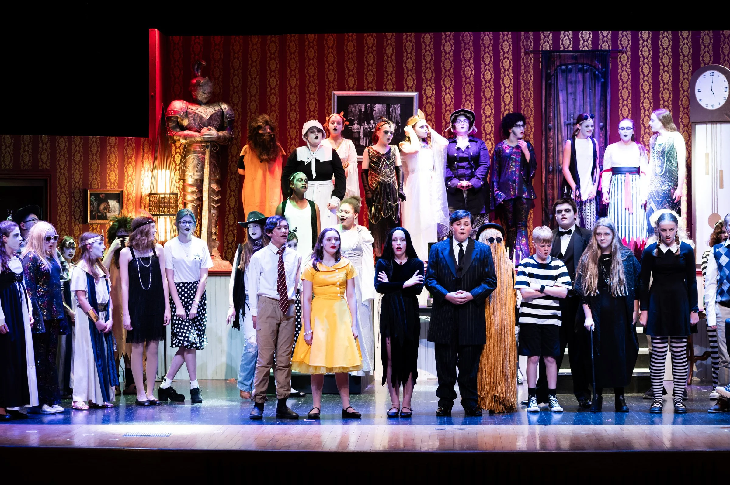 Children on stage during a school play, dressed in various costumes, with a decorated background and props.