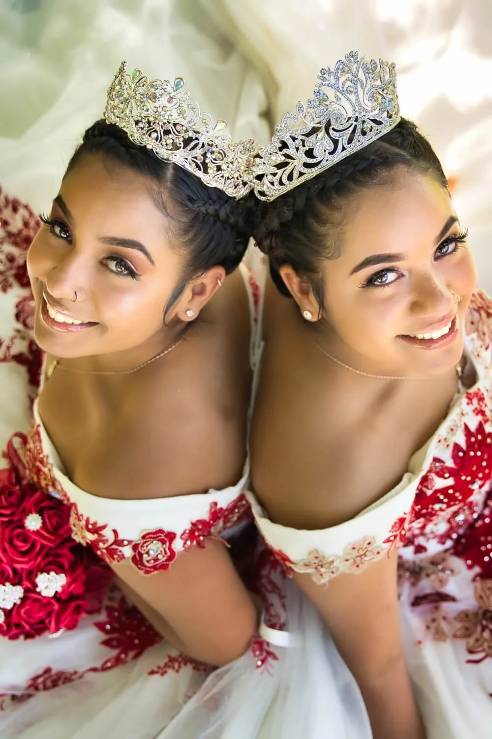 Two women wearing crowns and floral dresses, smiling and looking up at the camera.