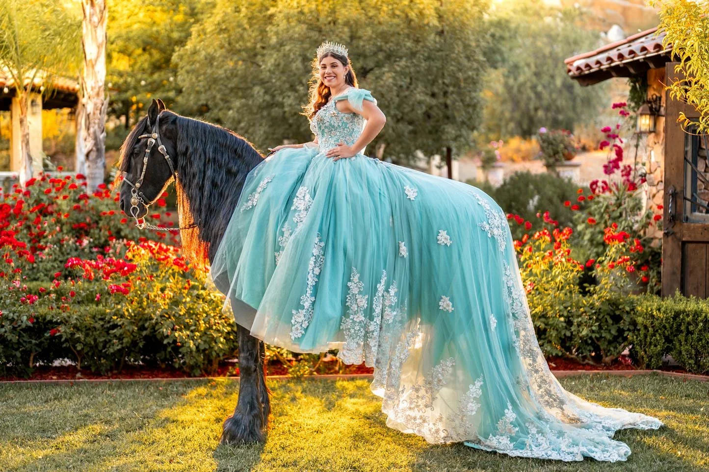 A woman in a blue princess dress riding a black horse in a garden with flowers and trees.