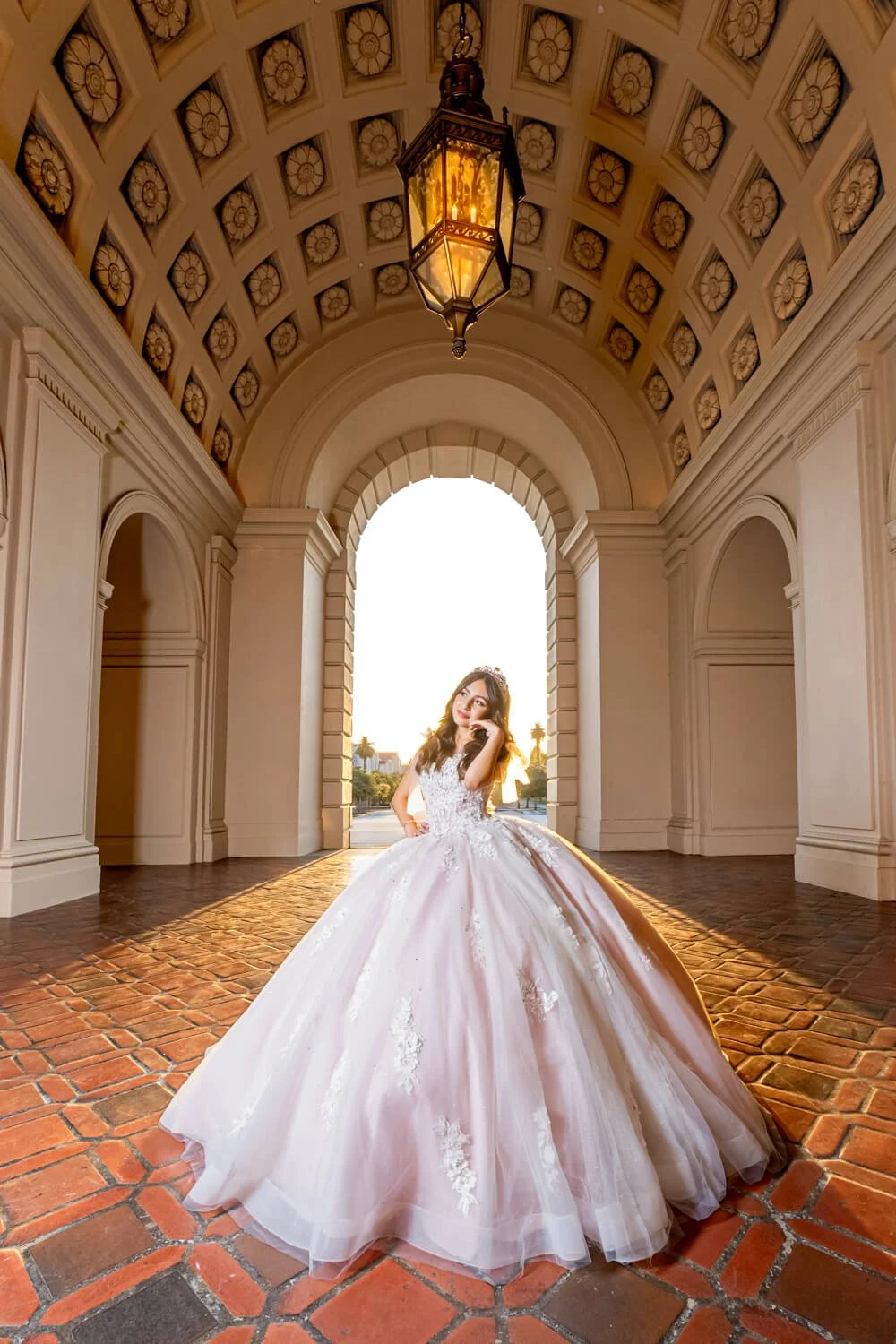 Young woman in a white ball gown standing in a grand arched entryway during sunset.