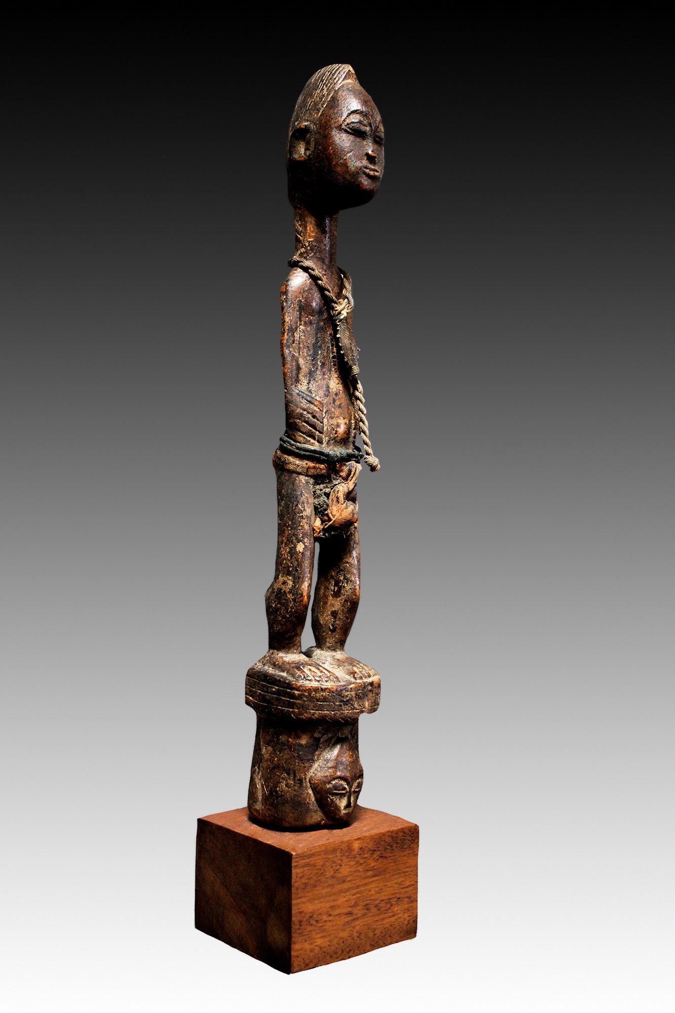 Baule figure stands on 2 ancestor faces.  www.gallerytribalar.com