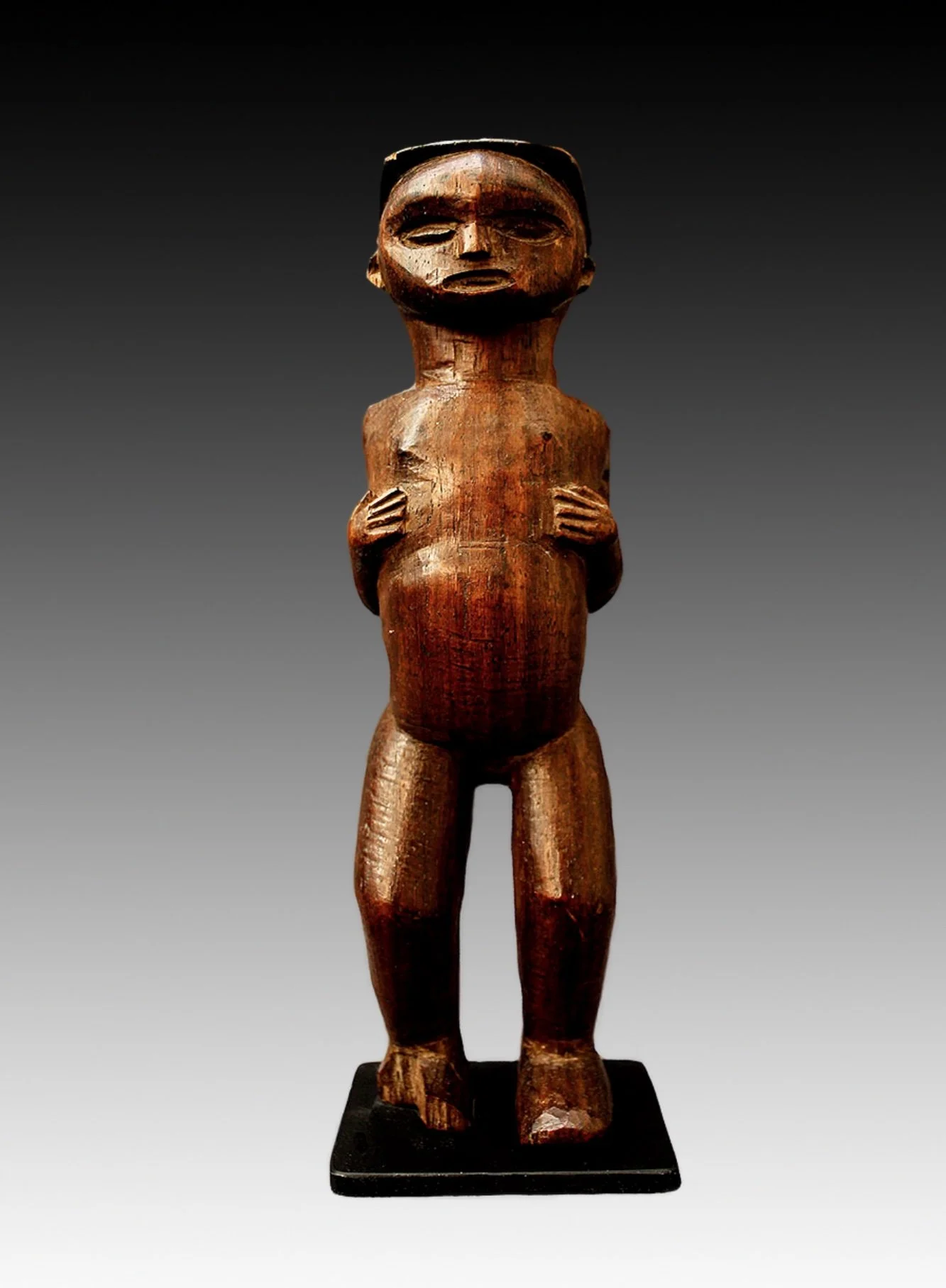 Chokwe figure, with naturalistic face, hands resting on it's chest with a reddish-brown patina.  www.gallerytribalart.com