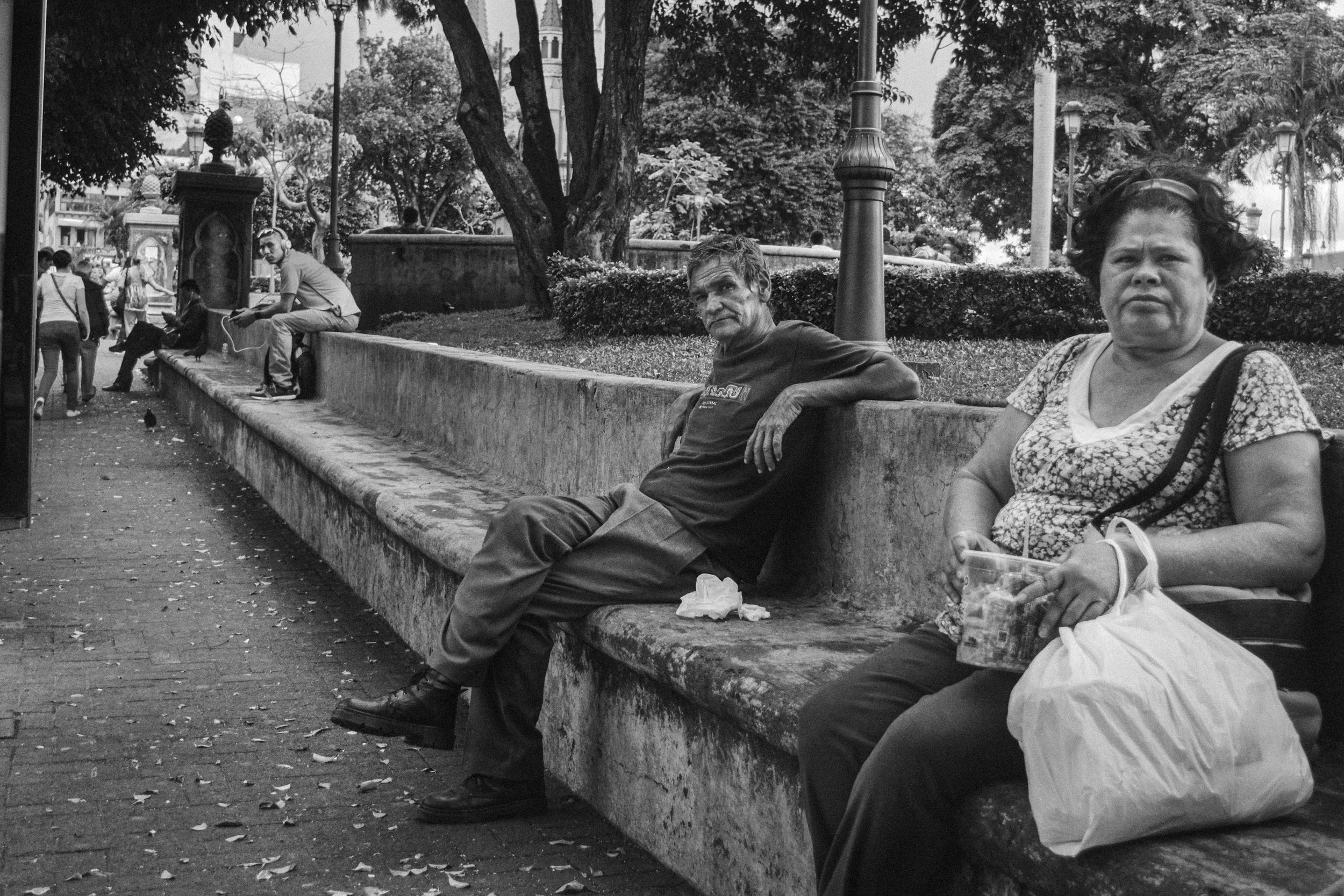 Three pedestrians sitting in park La Merced, just in front of the bus station. It has the particularity that nicaraguans tend to use this parc as their meeting point in the city center.