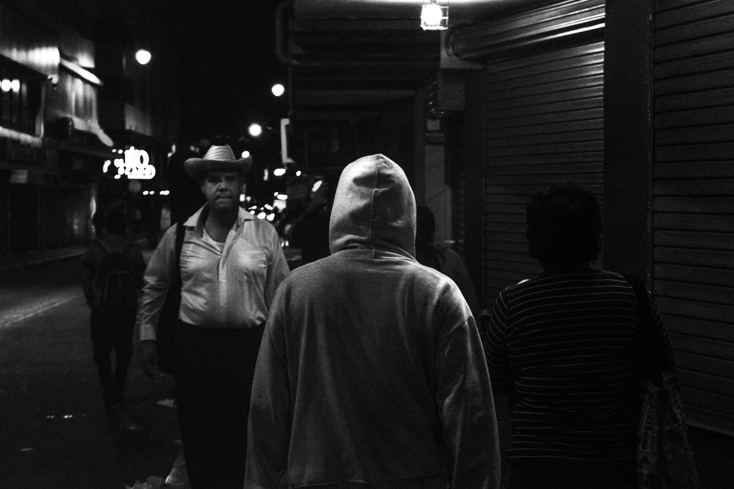 A man walking at night in Barrio Amón is being watched by other pedestrians.