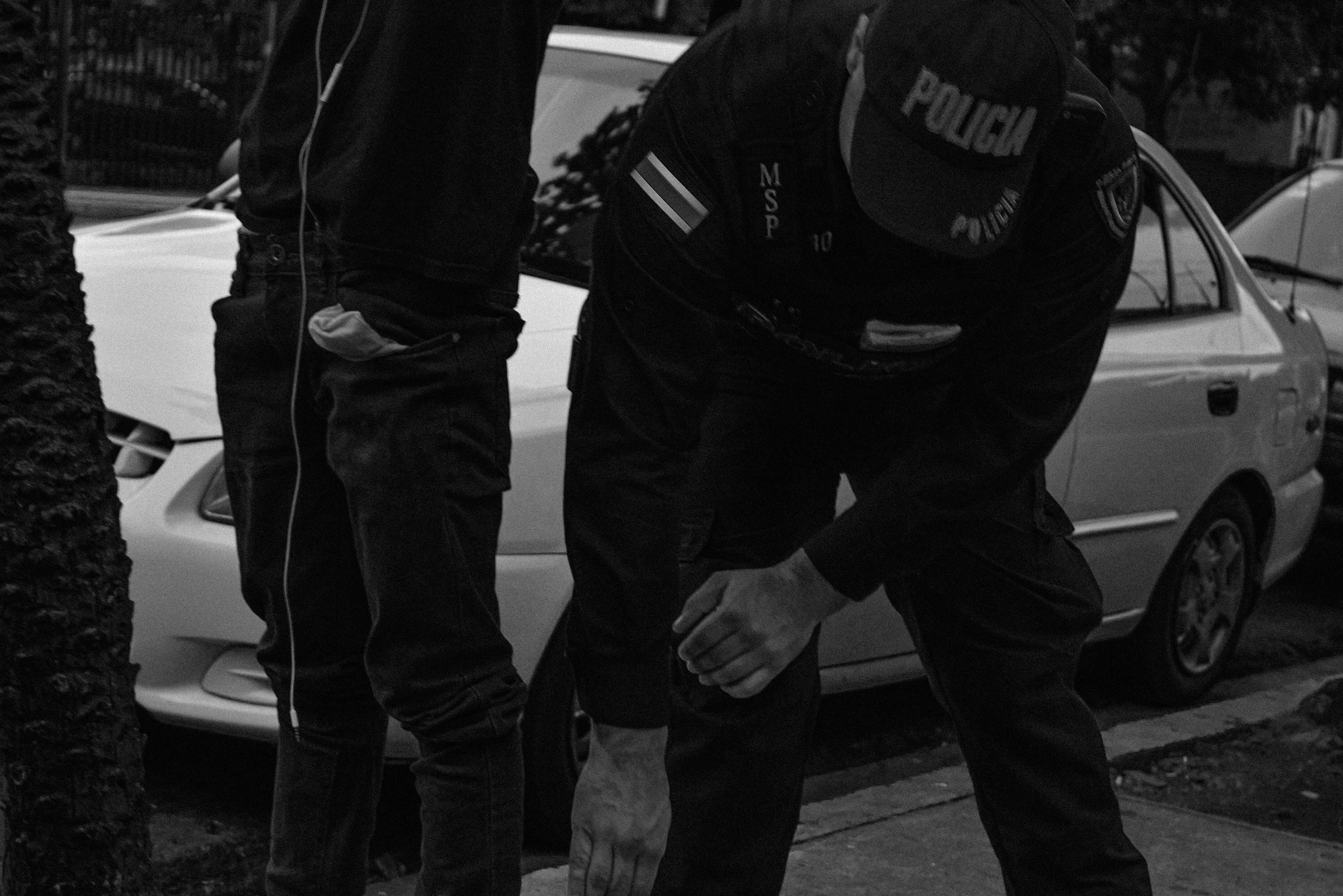 A police man searching a young boy for any illegal substance or weapon.