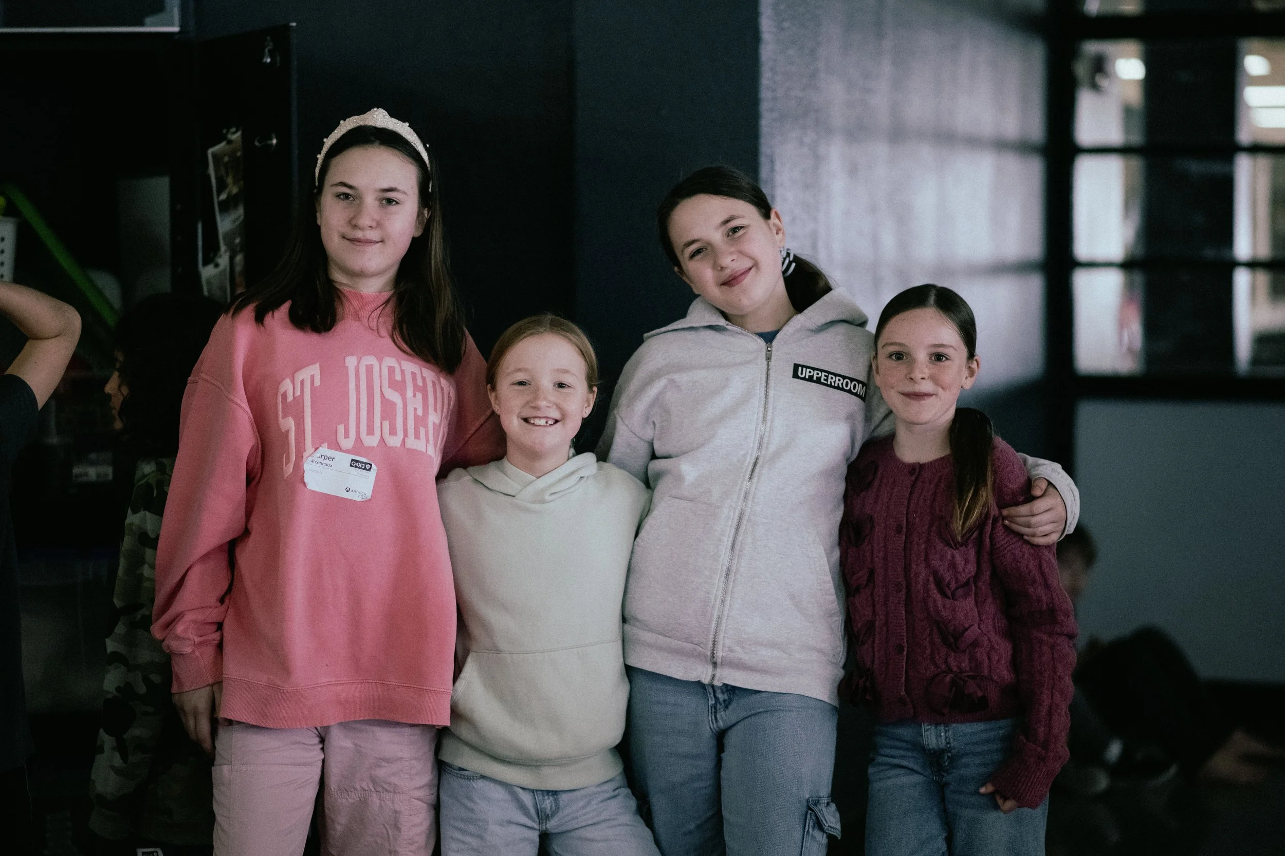 Two smiling kids sitting backward on colorful chairs, one in a red chair and the other in a blue chair, in a brightly lit room.