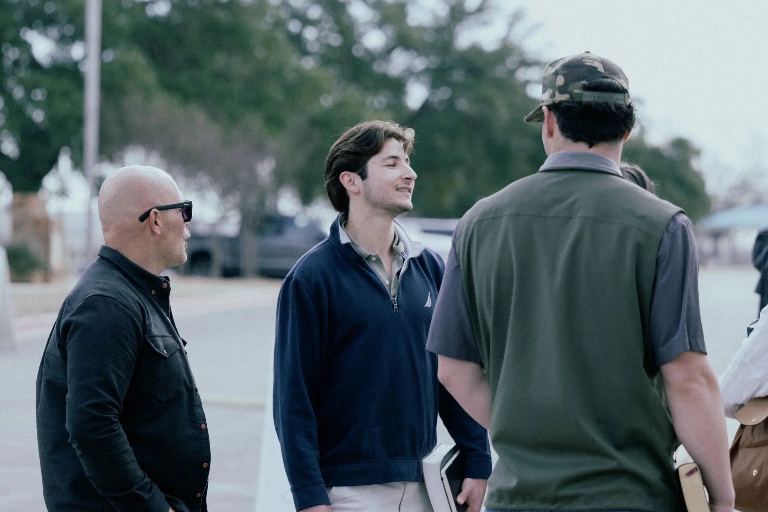 Three young women laughing together, holding books, outdoors.