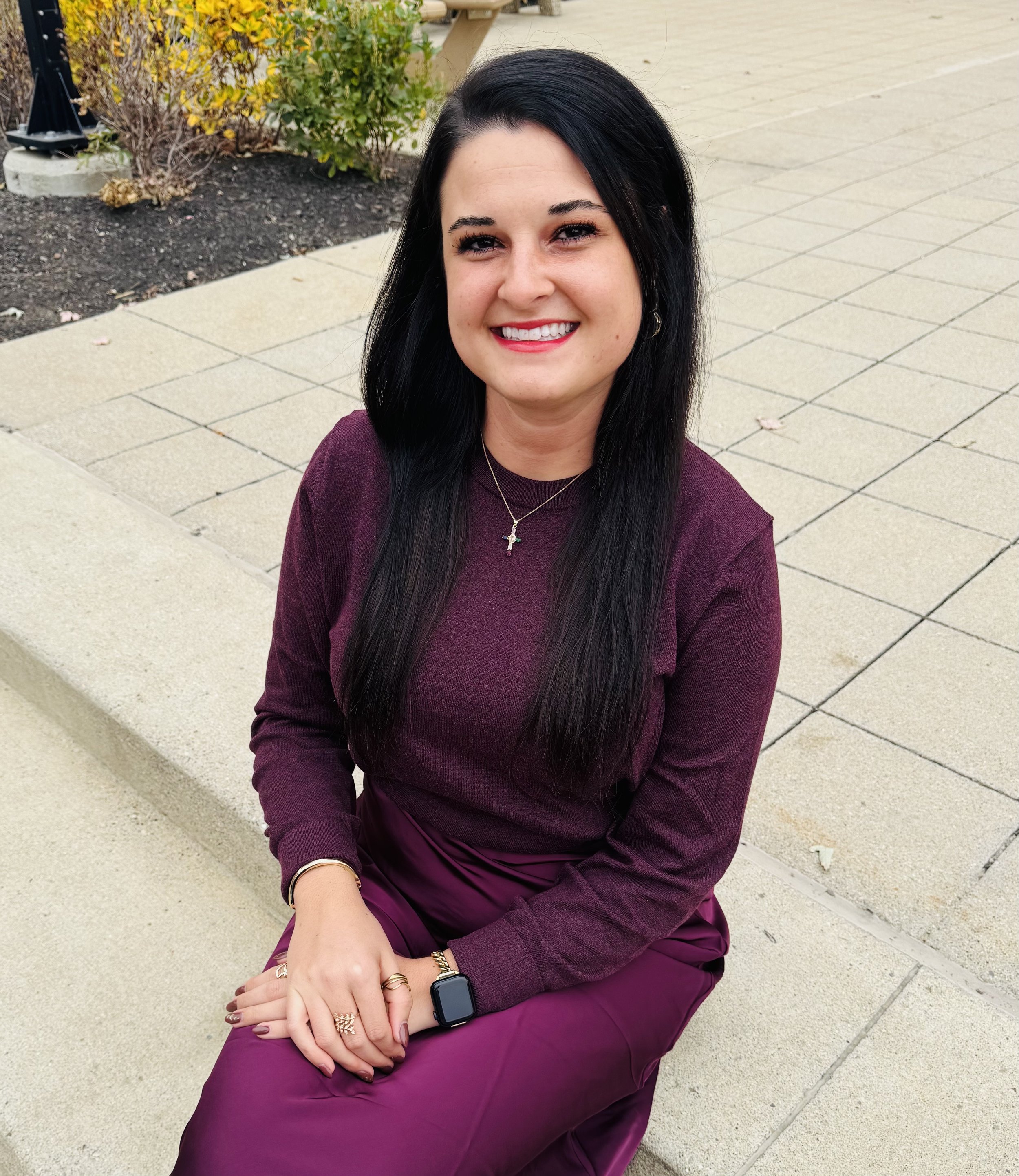 Woman in white blazer standing in front of colorful floral mural, smiling.