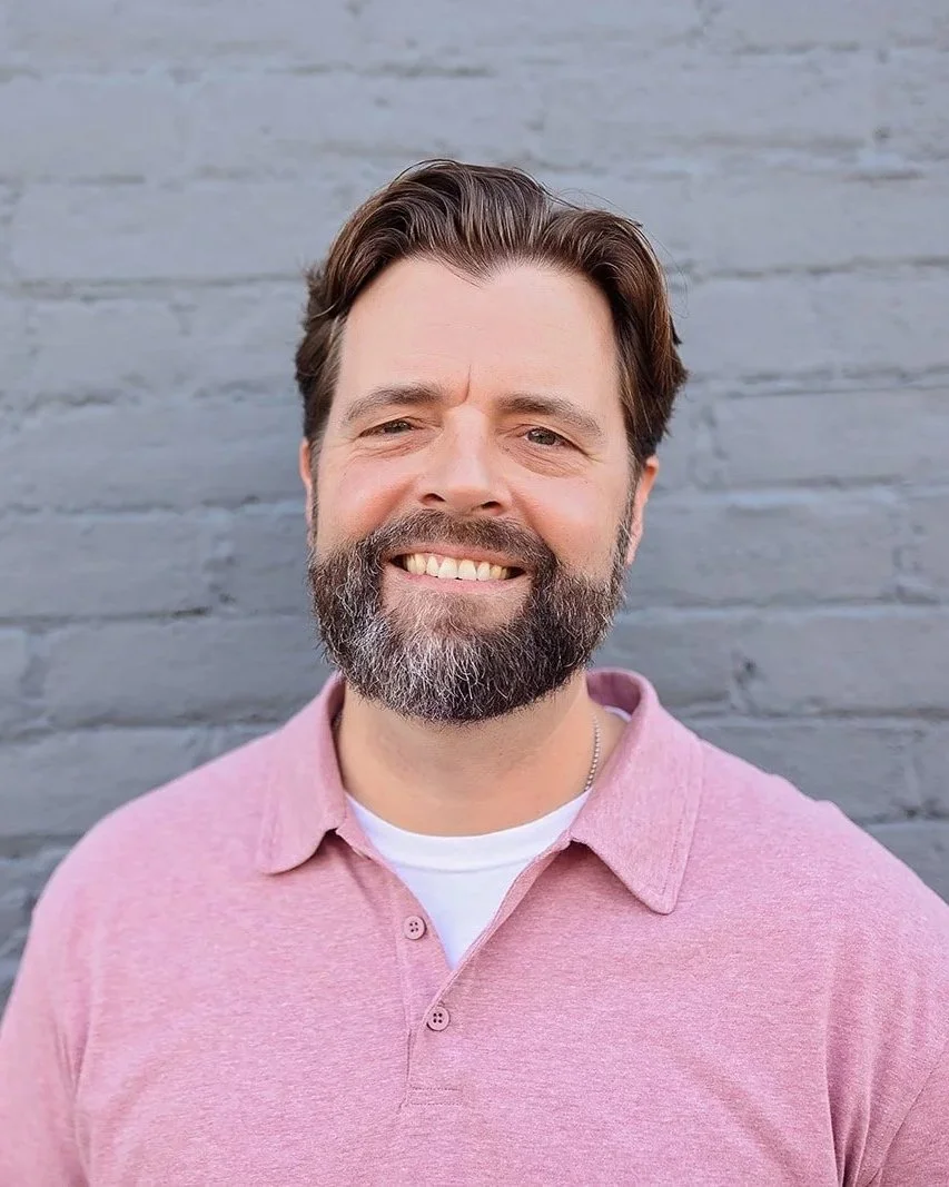 Smiling man in blue polo shirt in front of colorful floral mural.