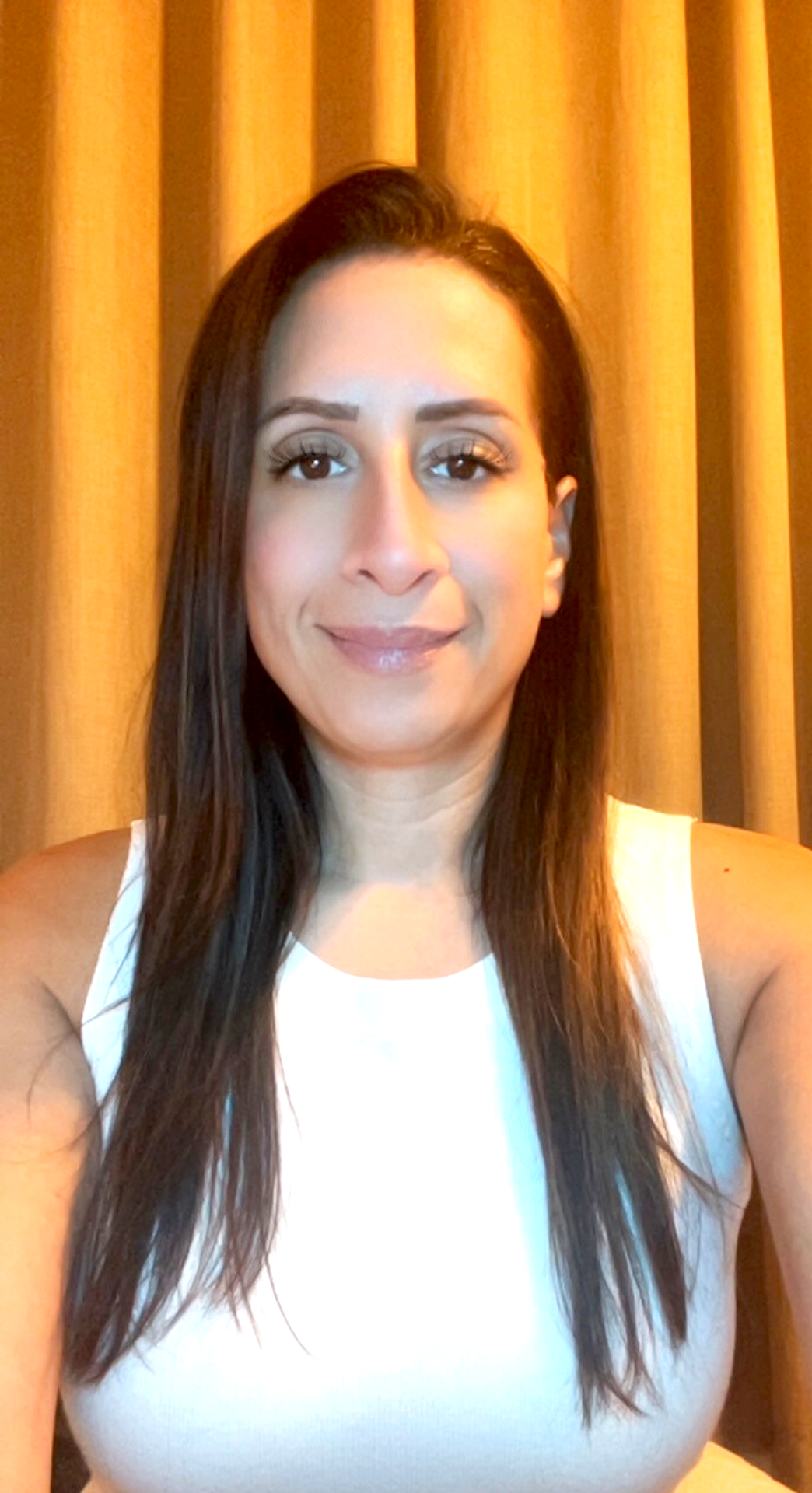 Woman smiling in front of a brick wall, wearing a blue sweater.