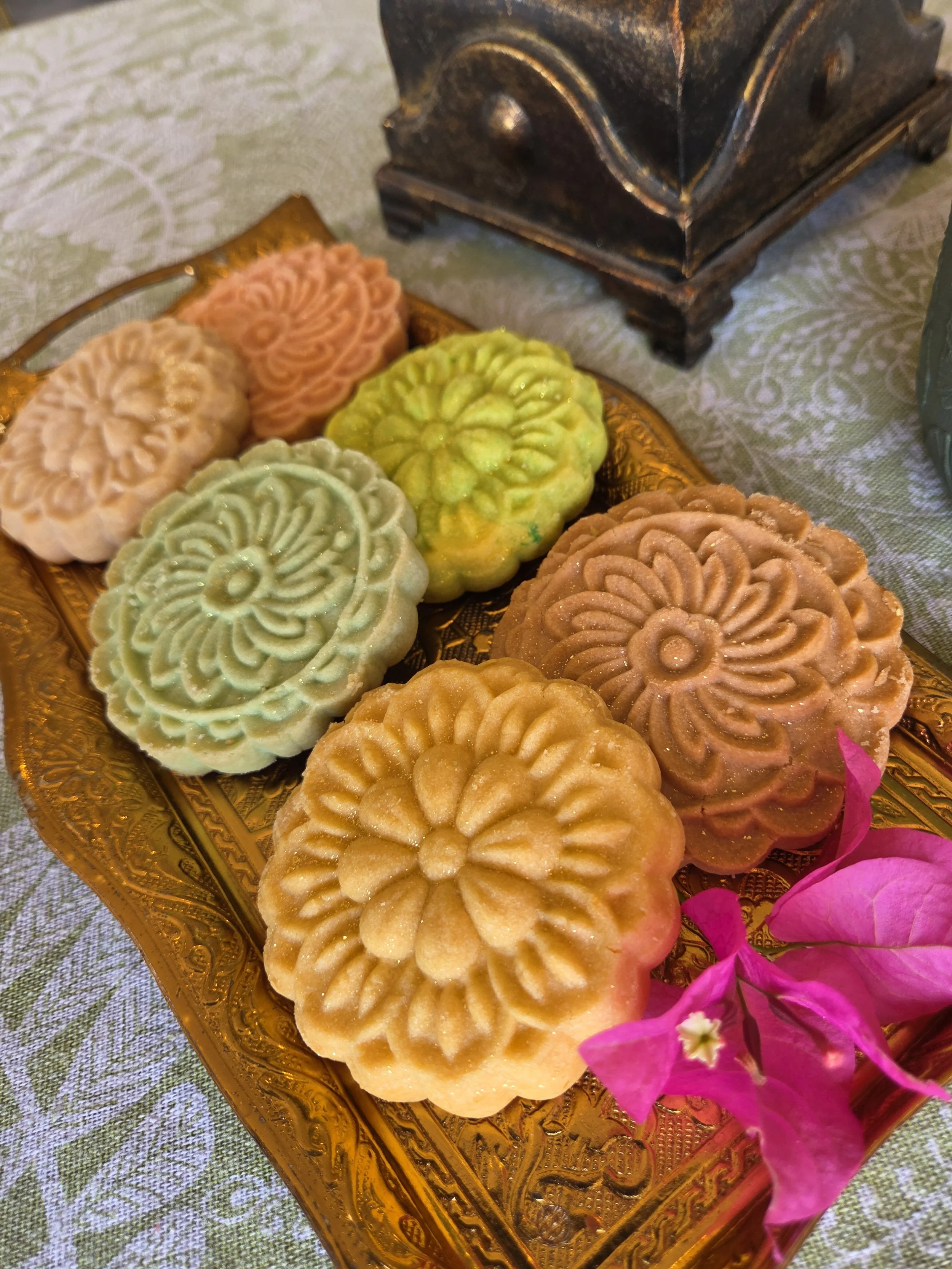 A plate with embossed brown flatbreads accompanied by colorful small purple, pink, and white flowers, placed on a patterned tablecloth.