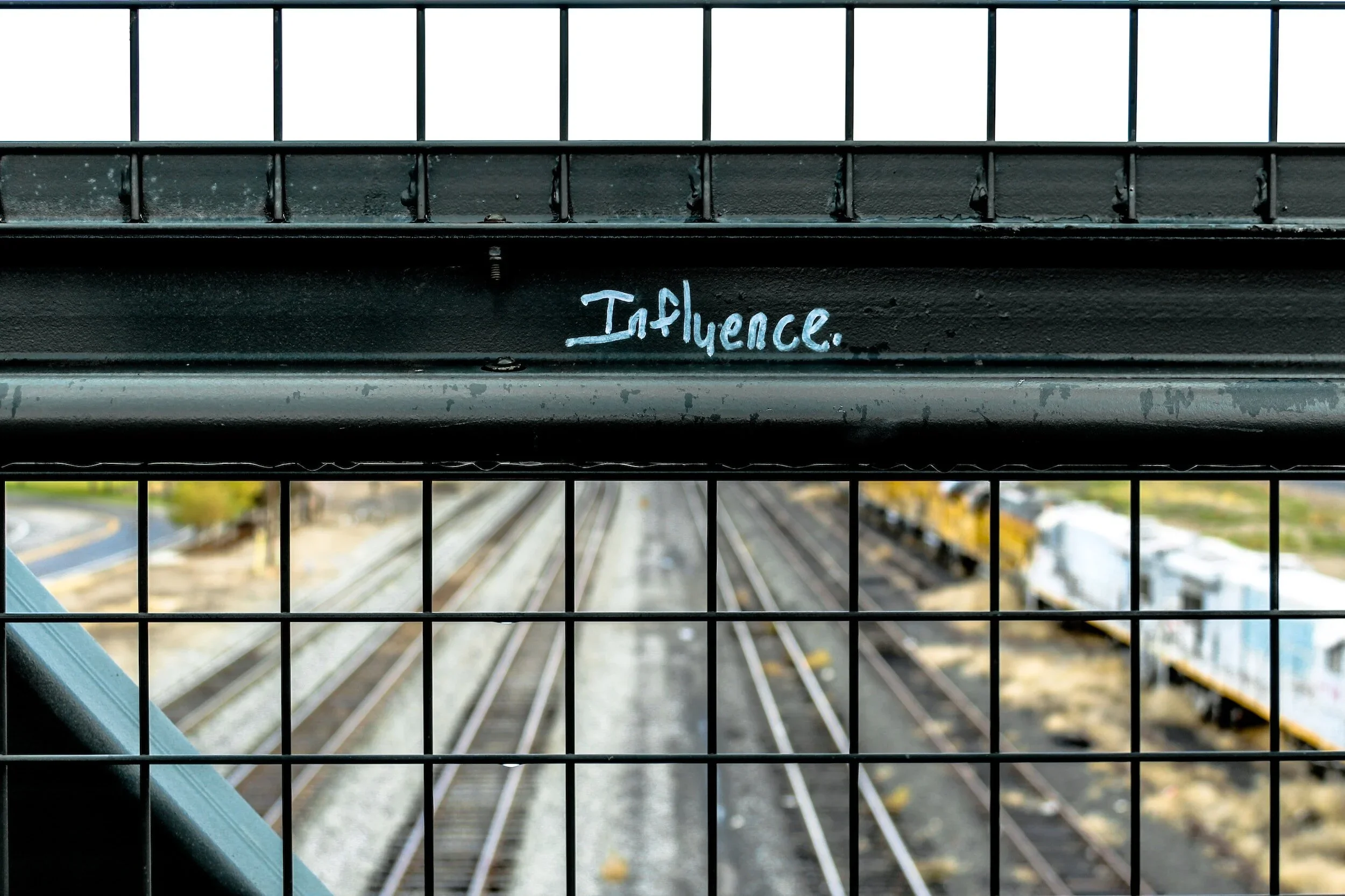 The word influence written on a fence over train tracks