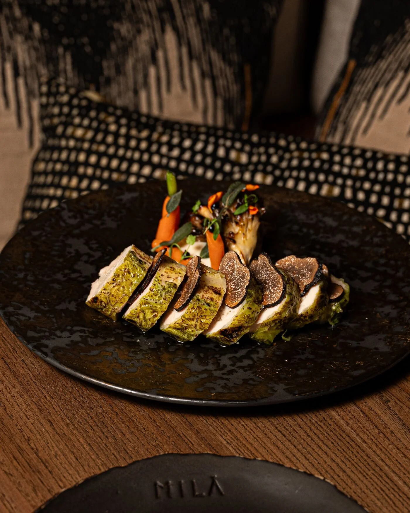 Gourmet sliced roasted meat with black truffle, grilled vegetables, carrots, and herbs on a black plate