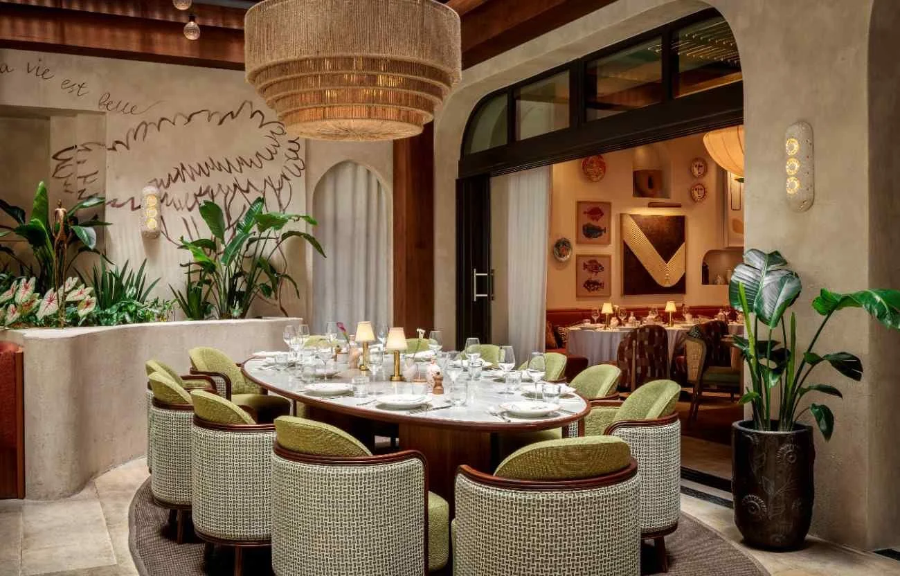 A large dining table at CLAUDIE for a big party, accompanied with green chairs and wine glasses on the table.