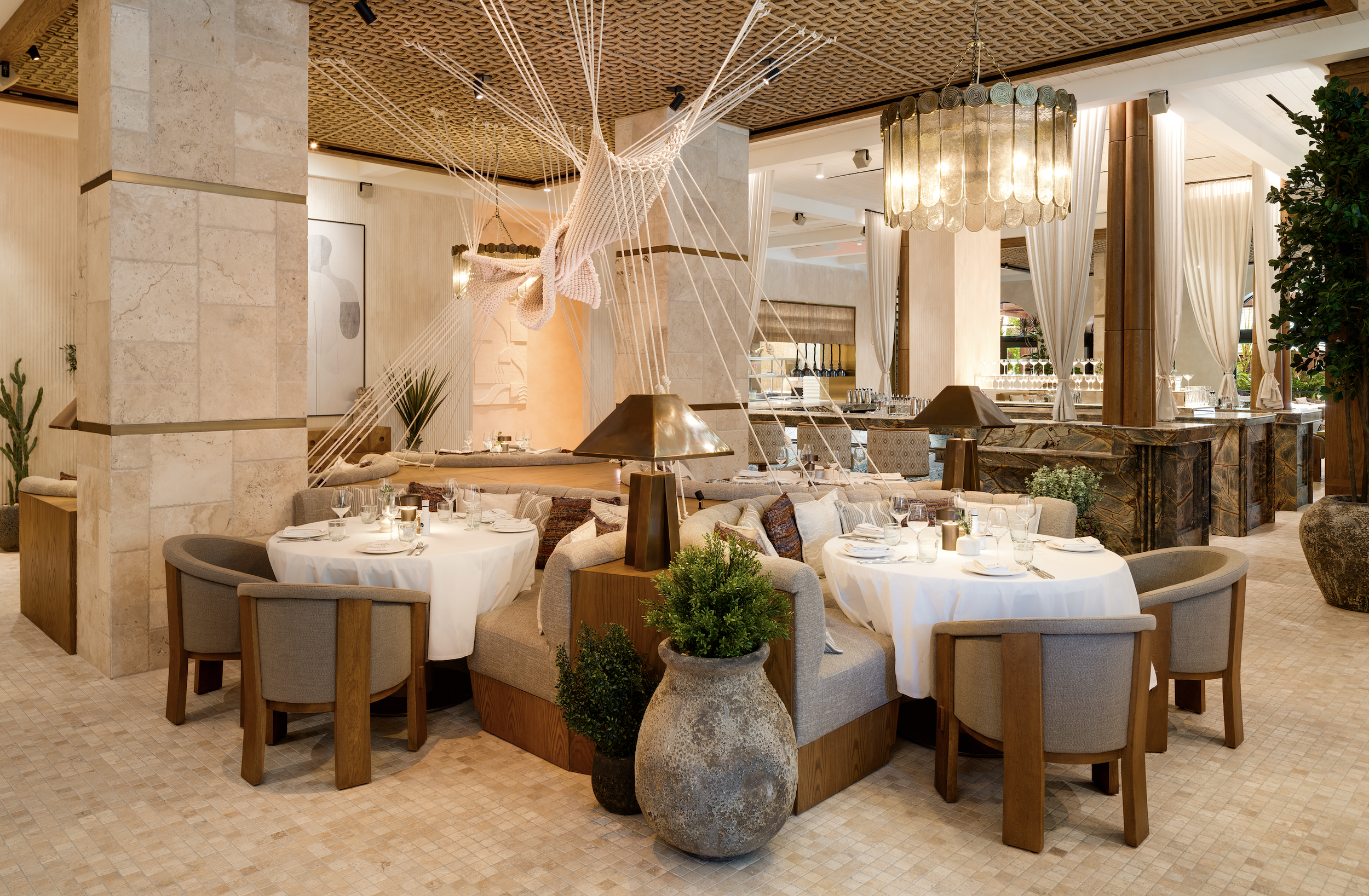 Elegant dining room at AVA Winter Park, decorated with an inspiration to the Mediterranean. Dining room has comfortable half booths, chairs, and tables with a unique artwork in the middle.