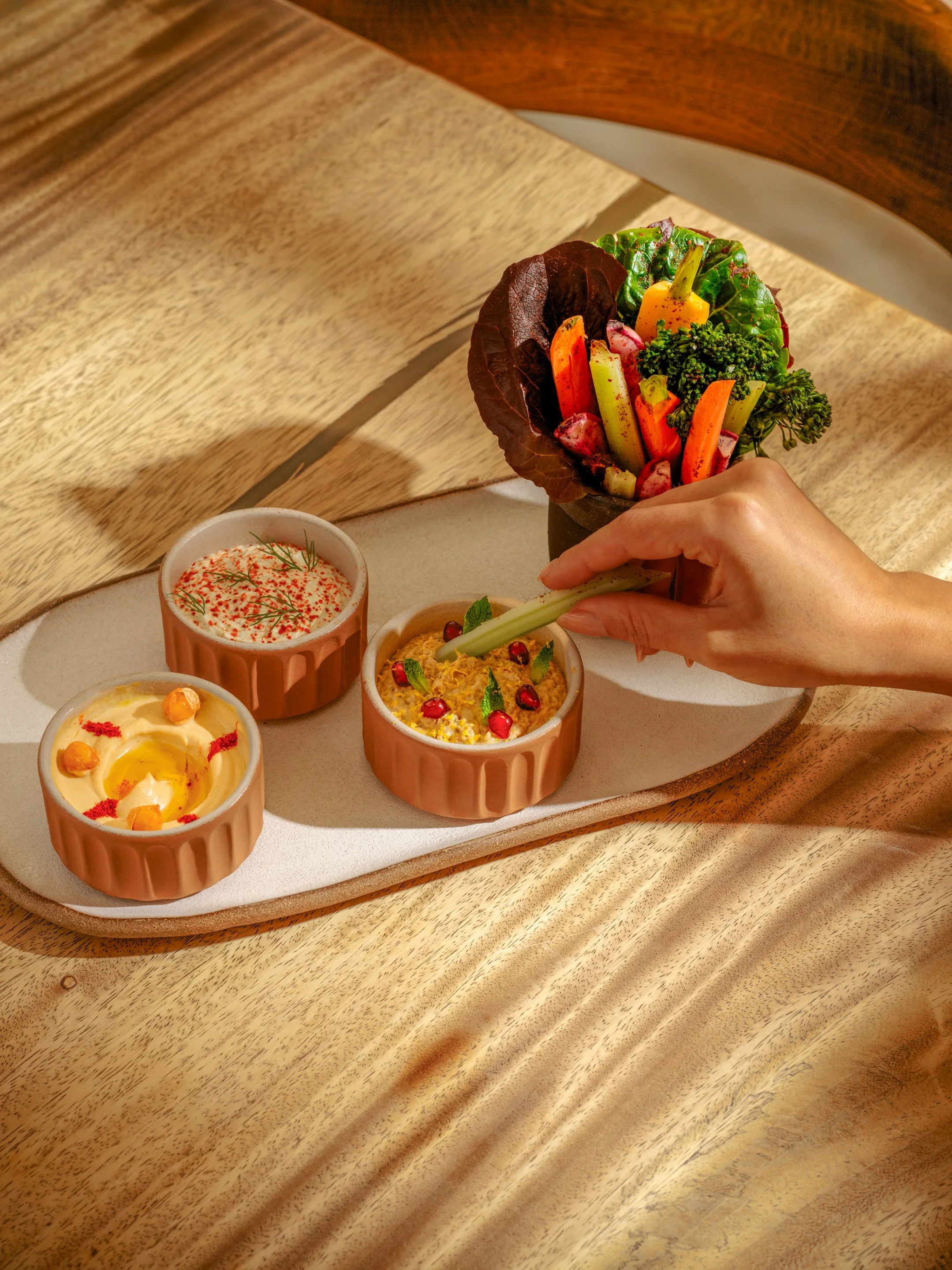 Three Greek Spreads with a side of refreshing vegetables on a table.
