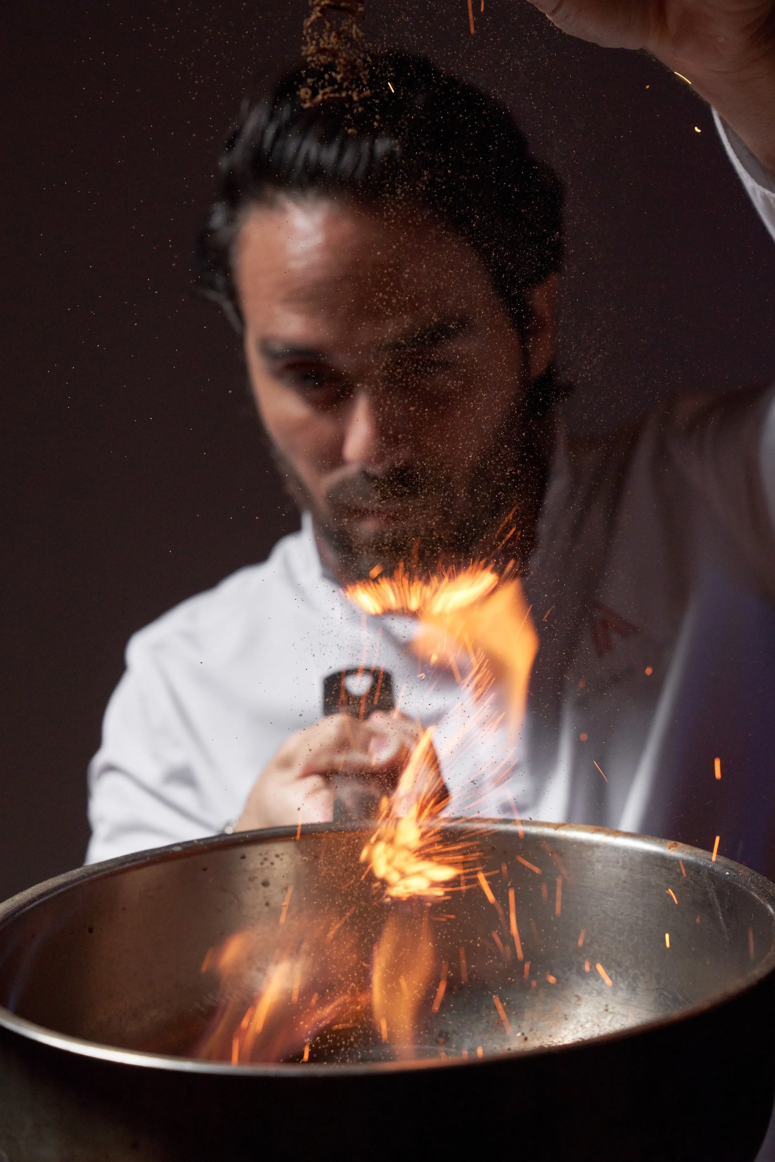A CASA NEOS chef cooking food in a silver pan, with fire on top.