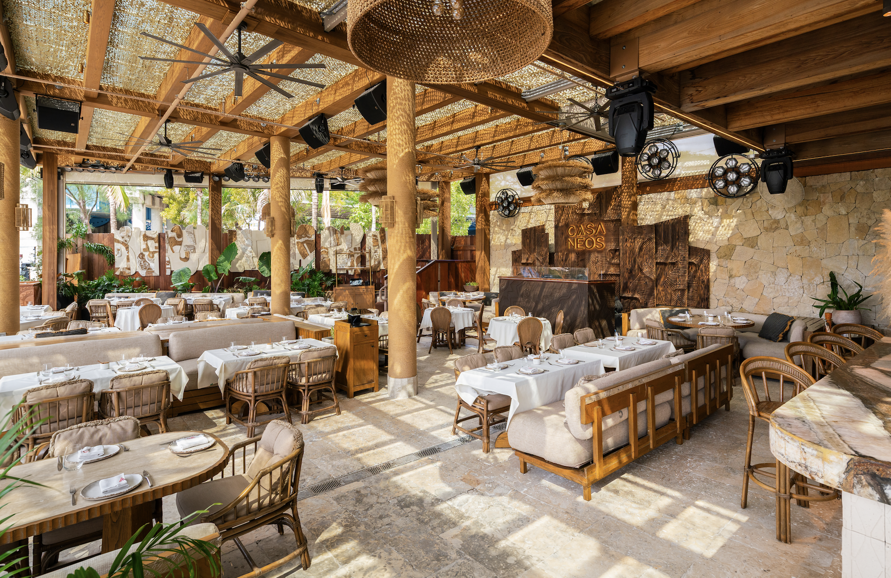 The dining setting of CASA NEOS, with comfortable chairs, couches and tables layed out with a DJ station in the back.