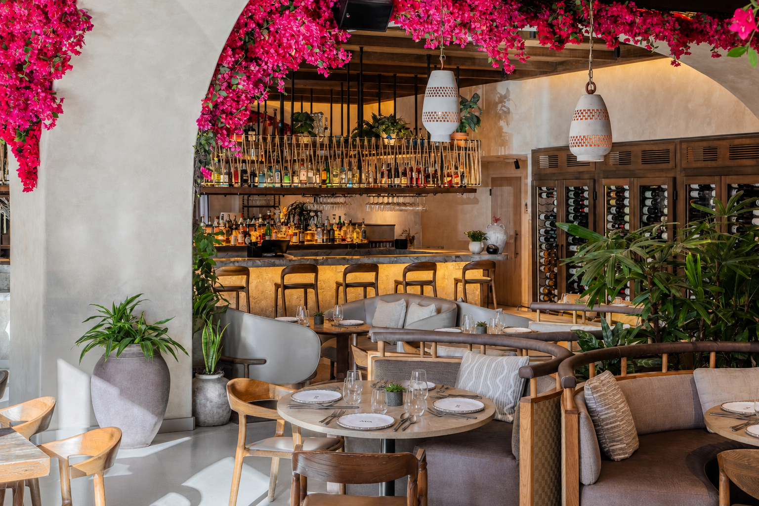 Upscale restaurant interior with a cocktail bar, wine display, tropical plants, and tables set for dining