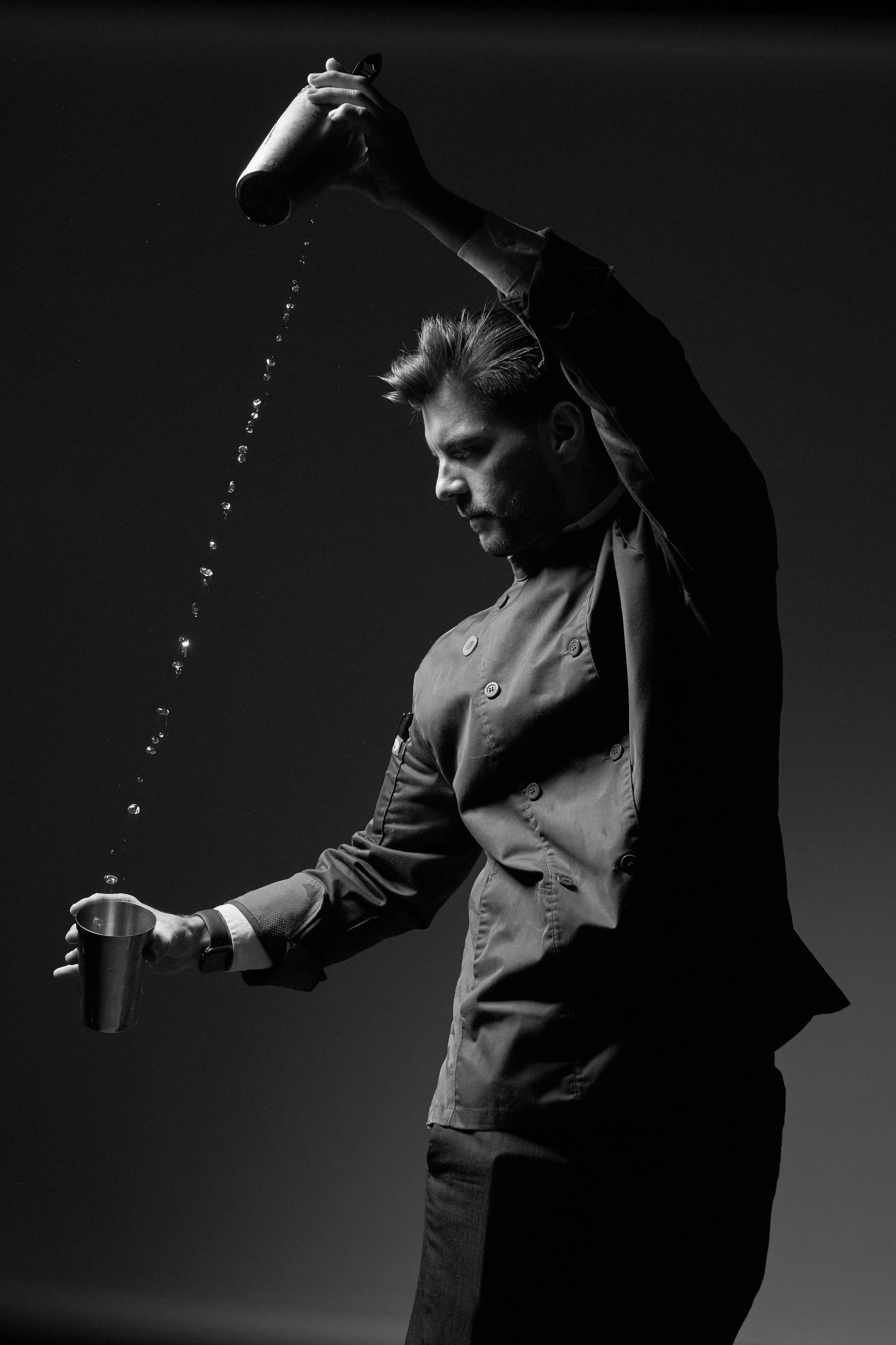 A bartender from CASA NEOS pouring a drink into a cup from a very high angle.