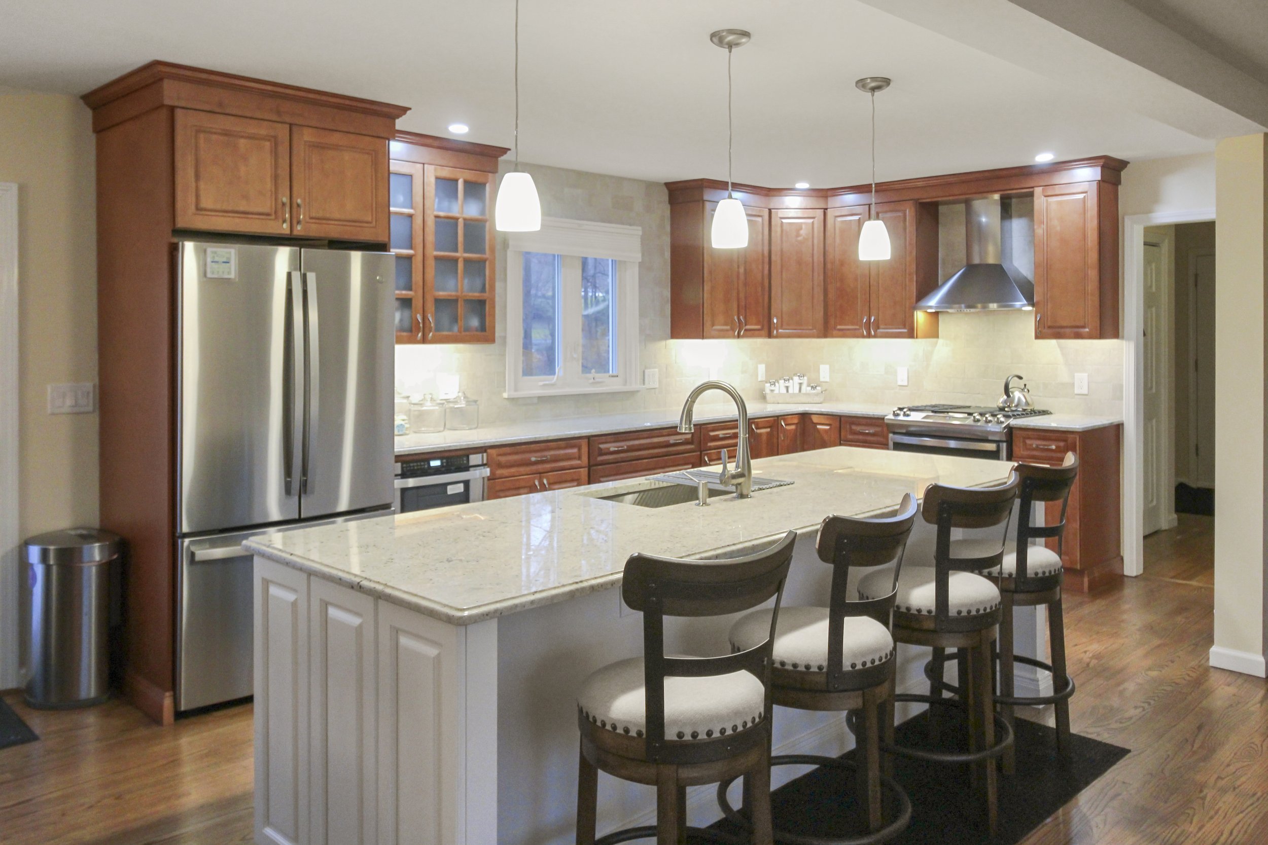 Modern kitchen with island, stainless steel appliances, pendant lights, wooden cabinets, and hardwood floor.