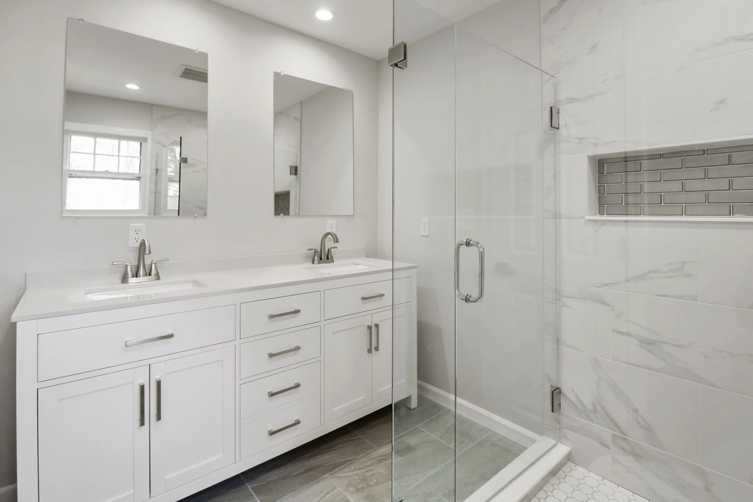 Modern bathroom with double sink vanity, white cabinets, large mirrors, and a glass-enclosed shower.